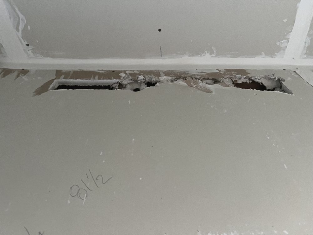 Damaged interior wall and ceiling with a long open crack and exposed area near the top.