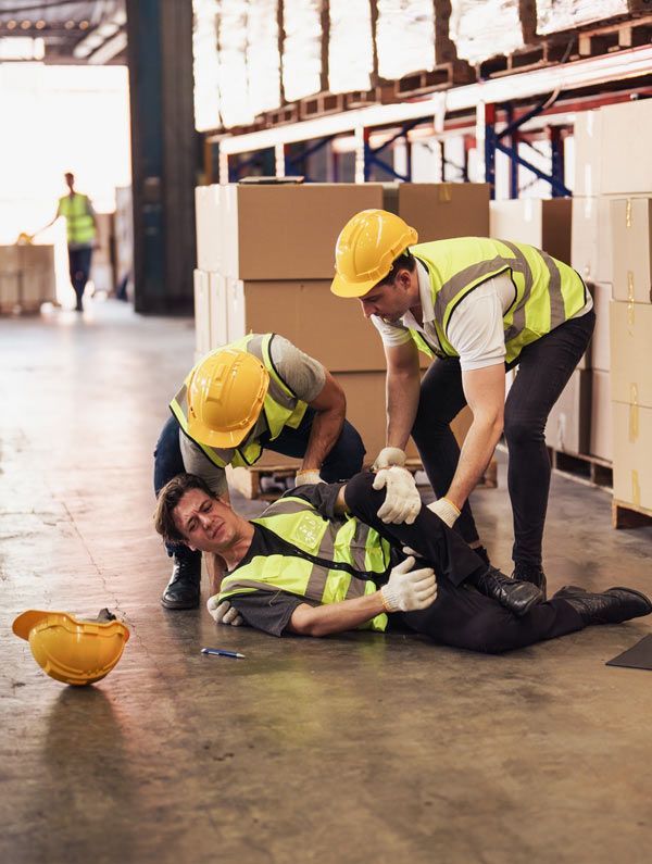 A group of construction workers are helping a man who has fallen on the floor in a warehouse. Ouimette, Goldstein, & Andrews, LLP - Trusted Workers' Compensation Representation in Nyack, NY