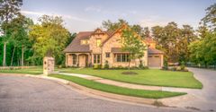 A large house is sitting on top of a lush green lawn in a residential neighborhood.