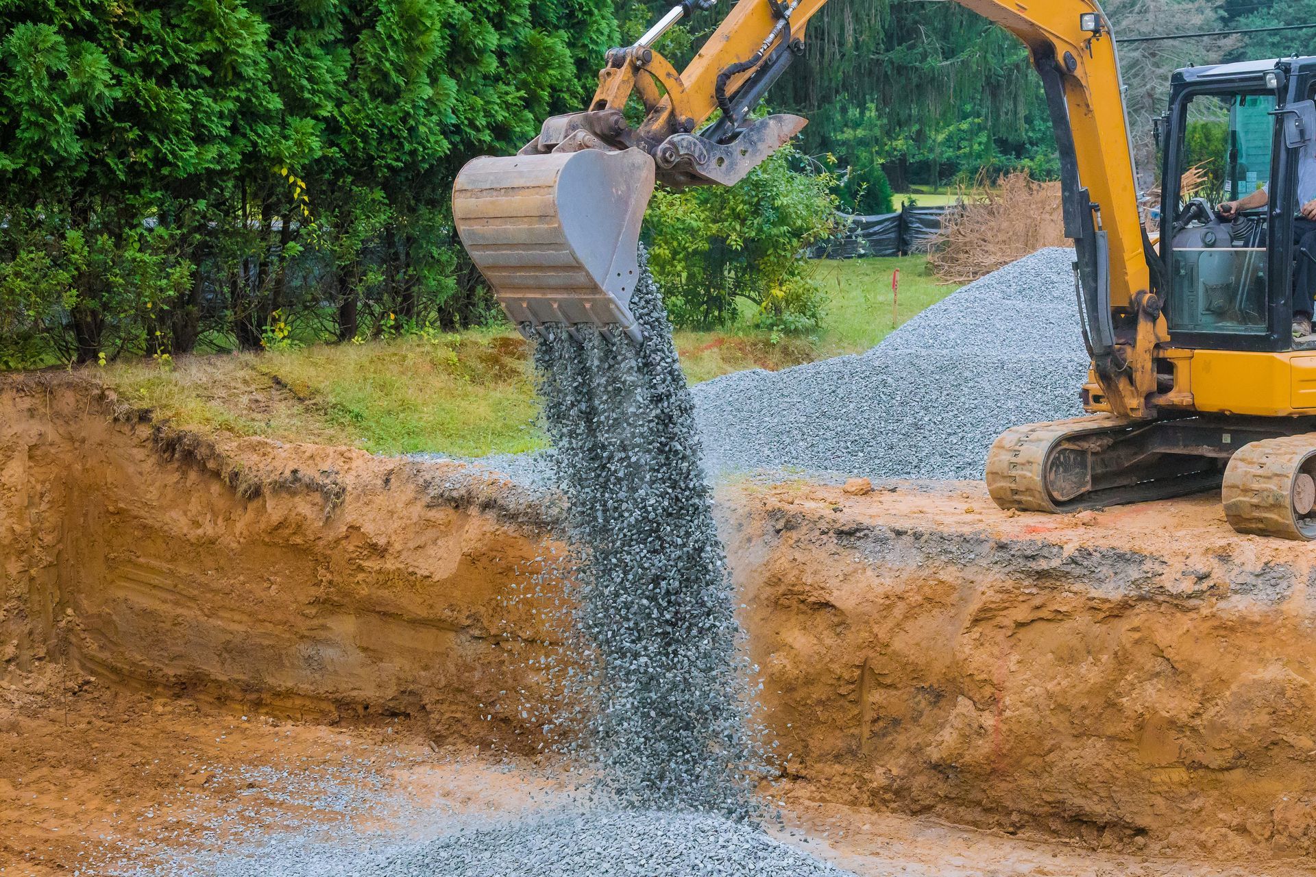 Une excavatrice déverse du gravier gris dans une tranchée de terre sur un chantier de construction.