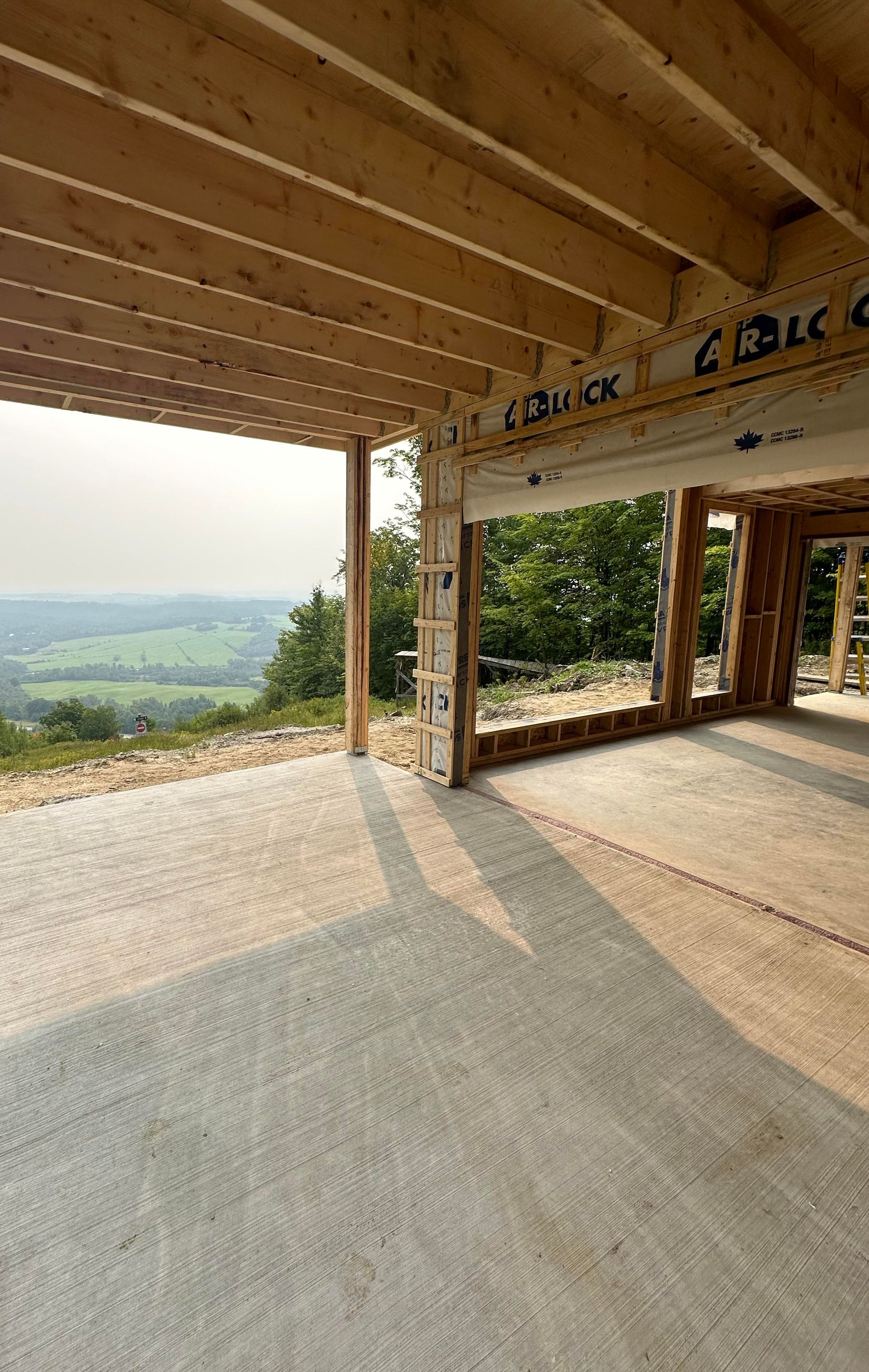 Vue intérieure d'un bâtiment en construction, donnant sur une vallée verdoyante. La lumière du soleil filtre à travers la porte.
