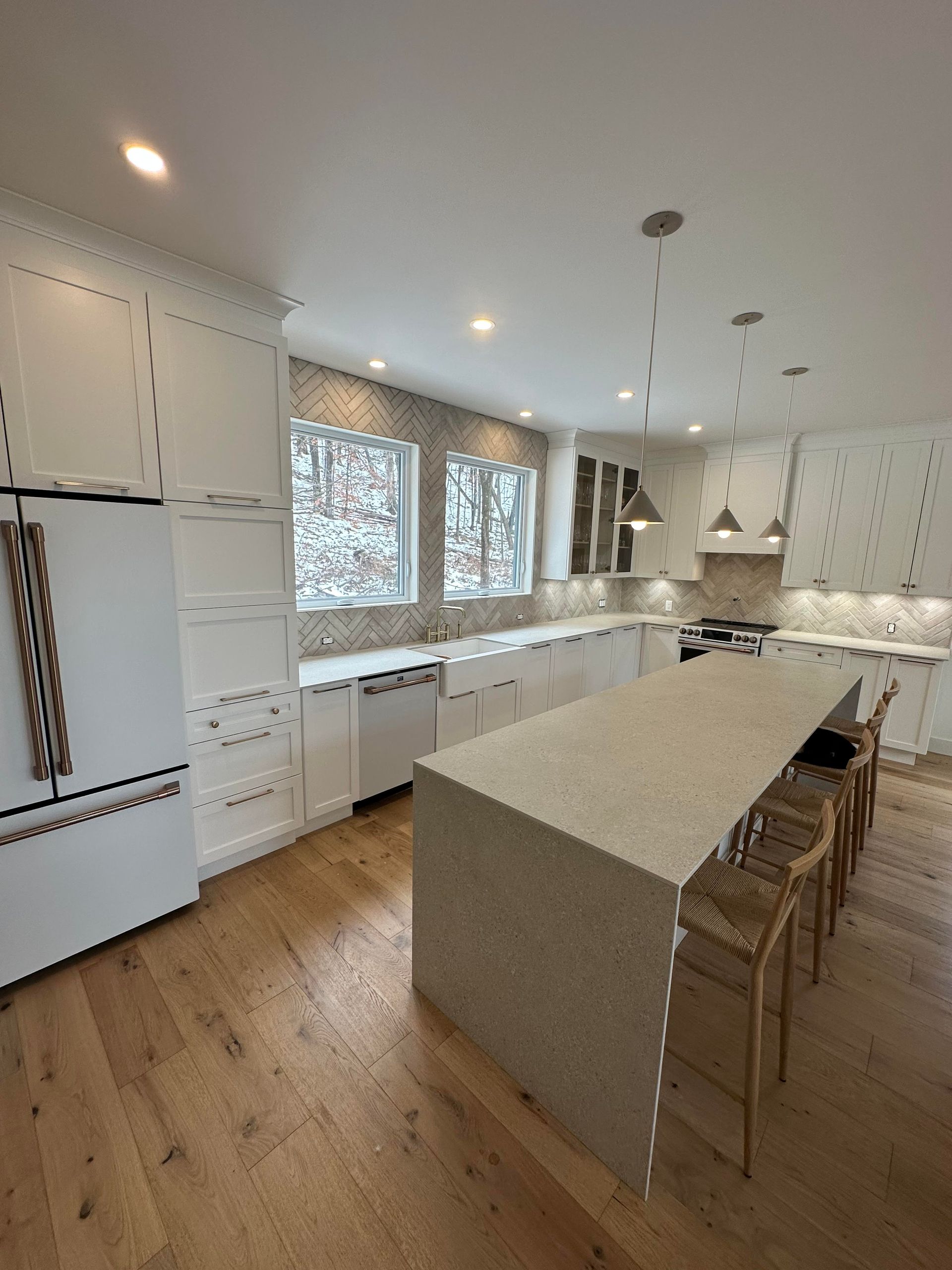 Cuisine moderne blanche avec îlot central, parquet et deux fenêtres.