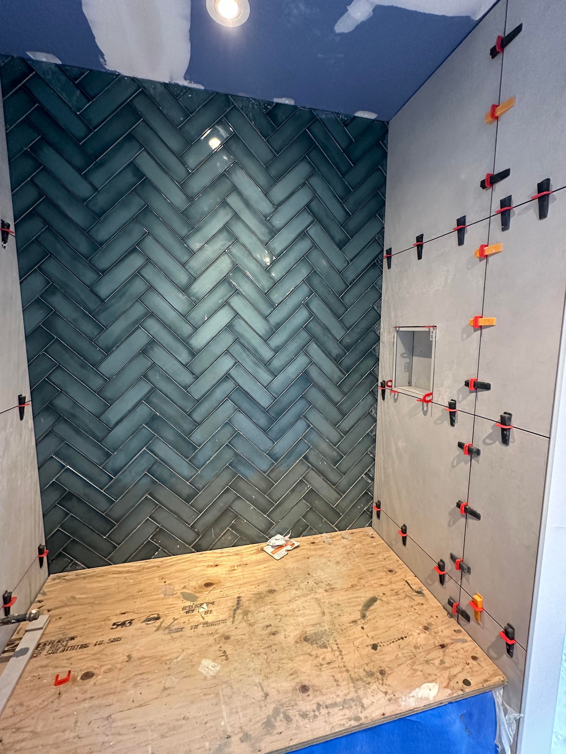 Douche avec mur d'accent en carrelage à chevrons bleu-vert, murs non finis, sol en contreplaqué, clips de nivellement.