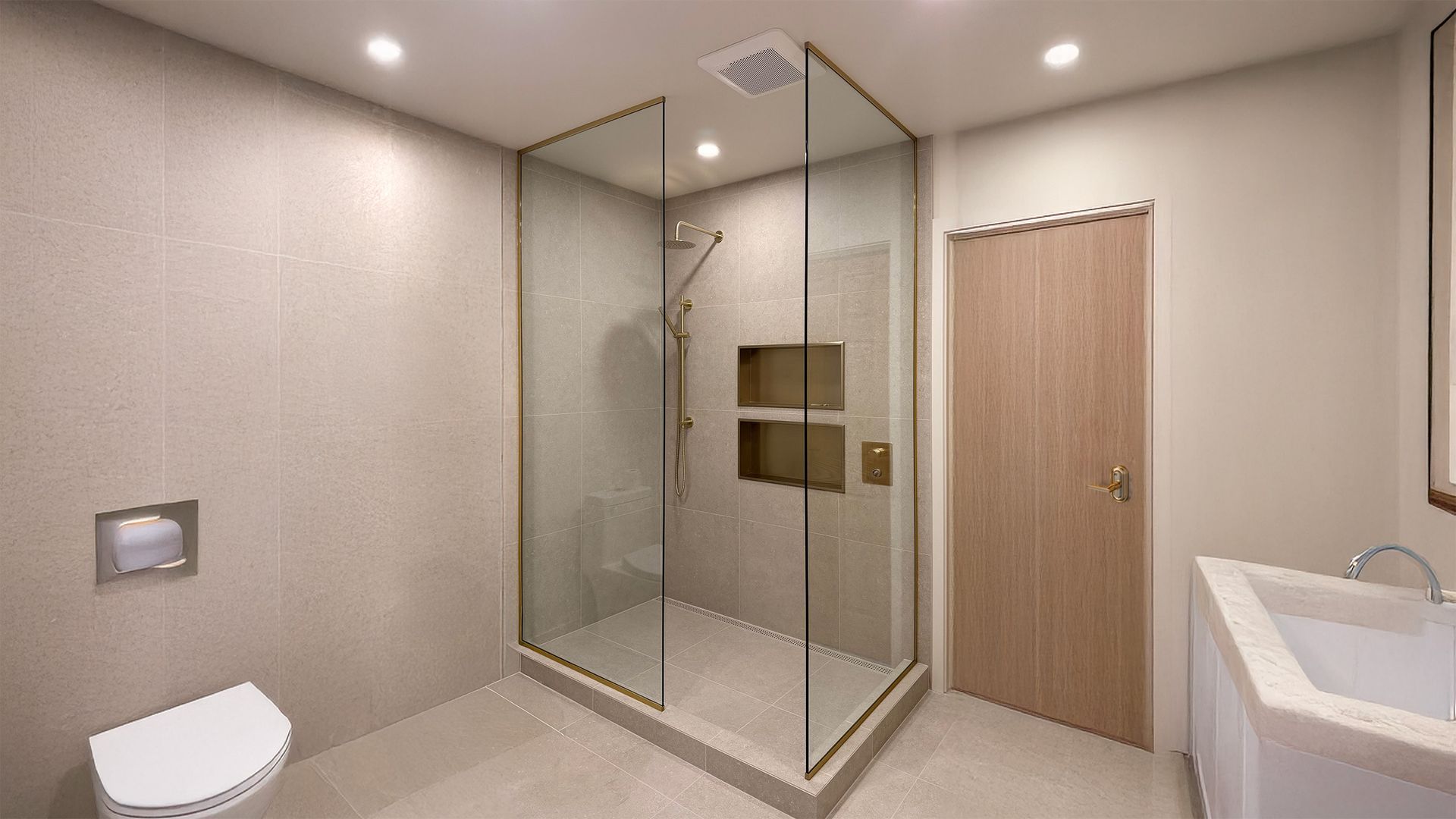 Salle de bains moderne avec douche en verre, porte en bois, toilettes, lavabo et murs carrelés beiges sous éclairage encastré