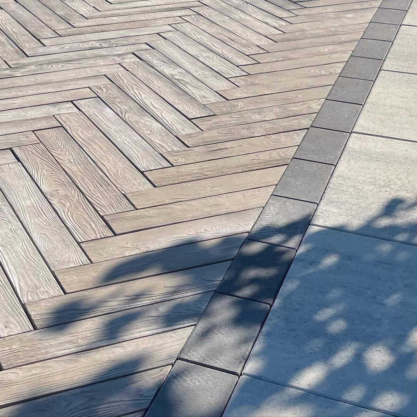 Des pavés gris clair à motif en chevrons laissent place à des pavés gris lisses, jouant sur les ombres.