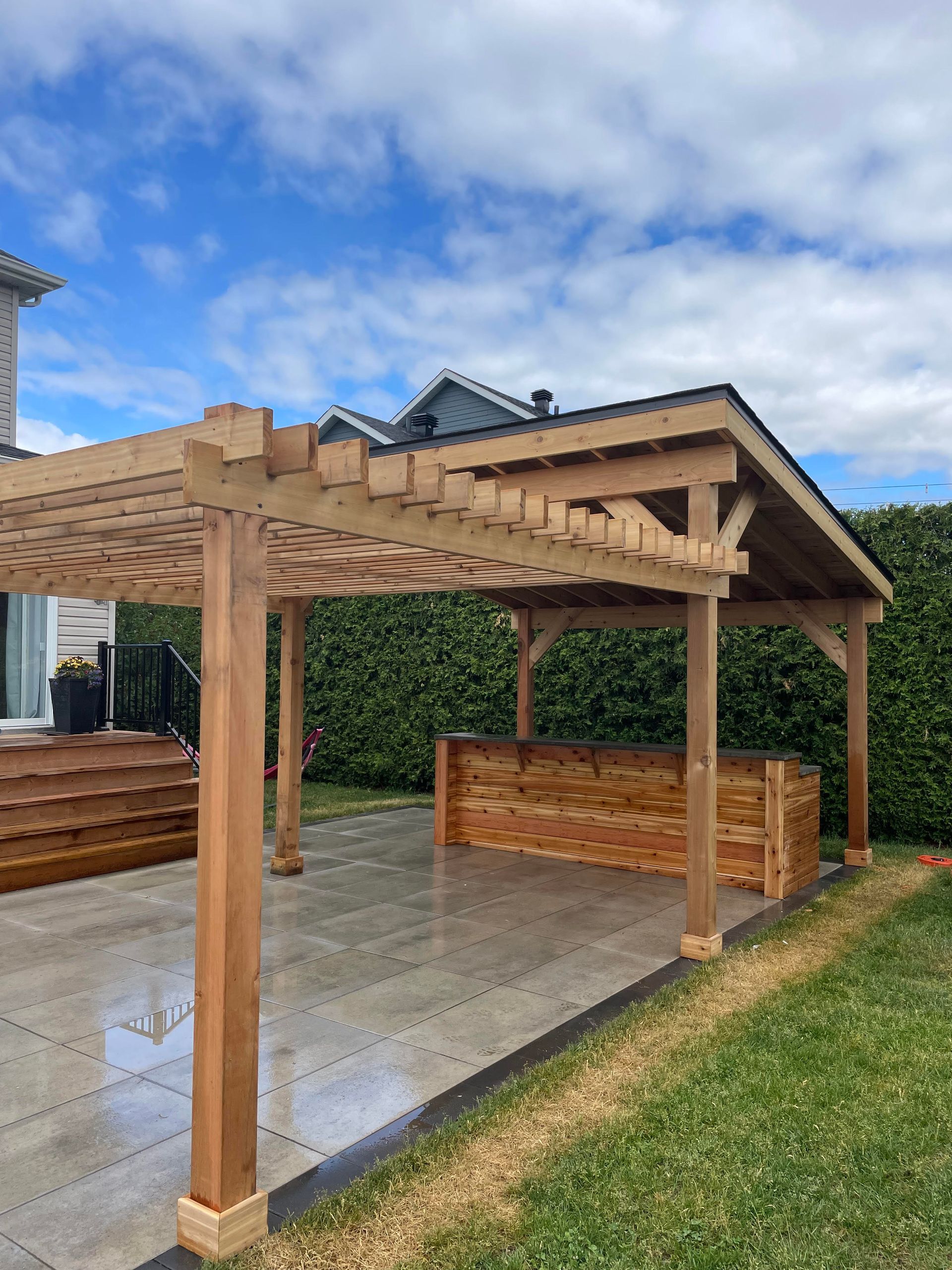Pergola en bois avec un bar sur une terrasse, sous un ciel bleu.