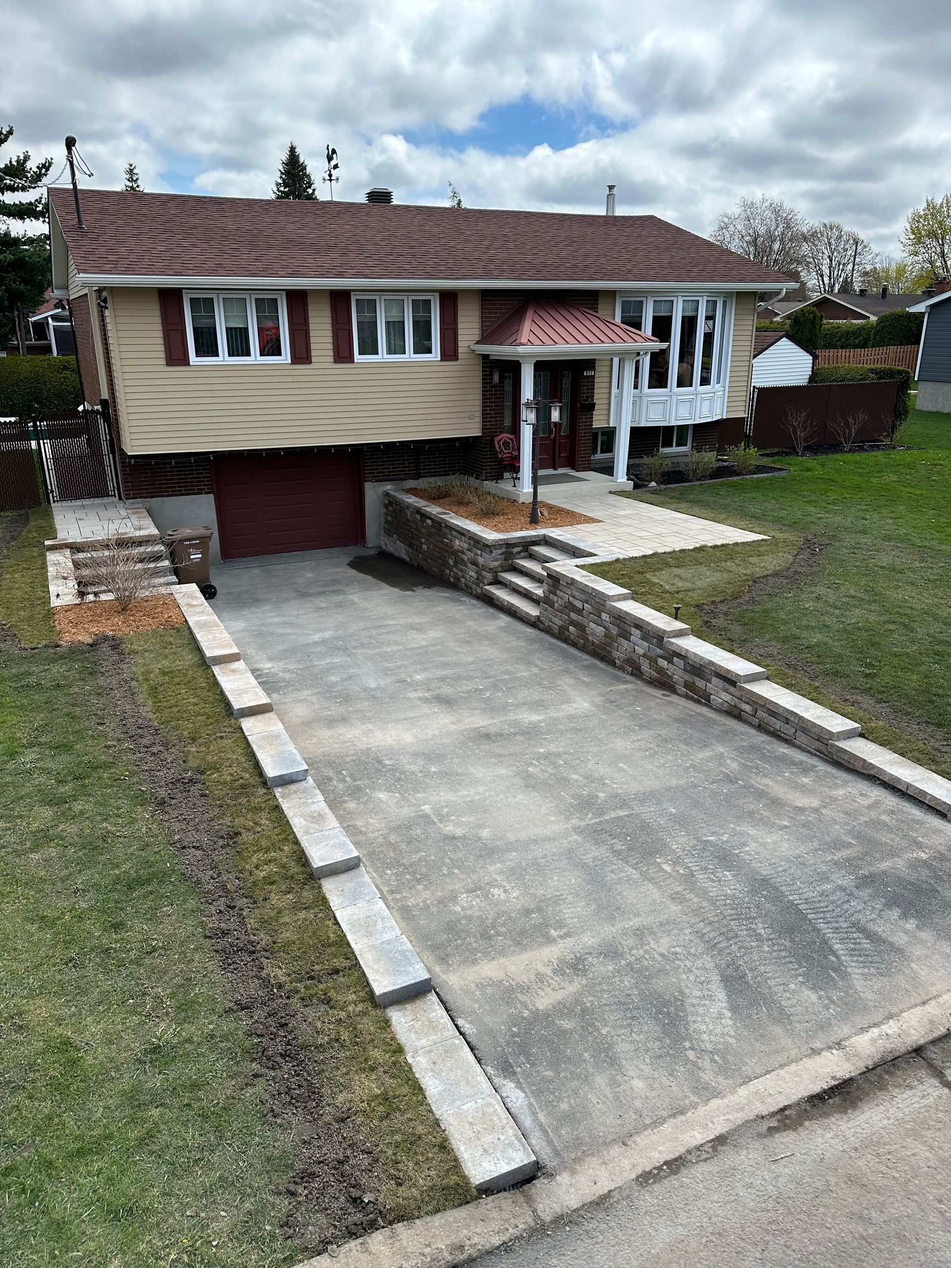 Maison beige à deux étages avec toit rouge et garage. Allée en béton en pente douce menant à l'entrée principale.