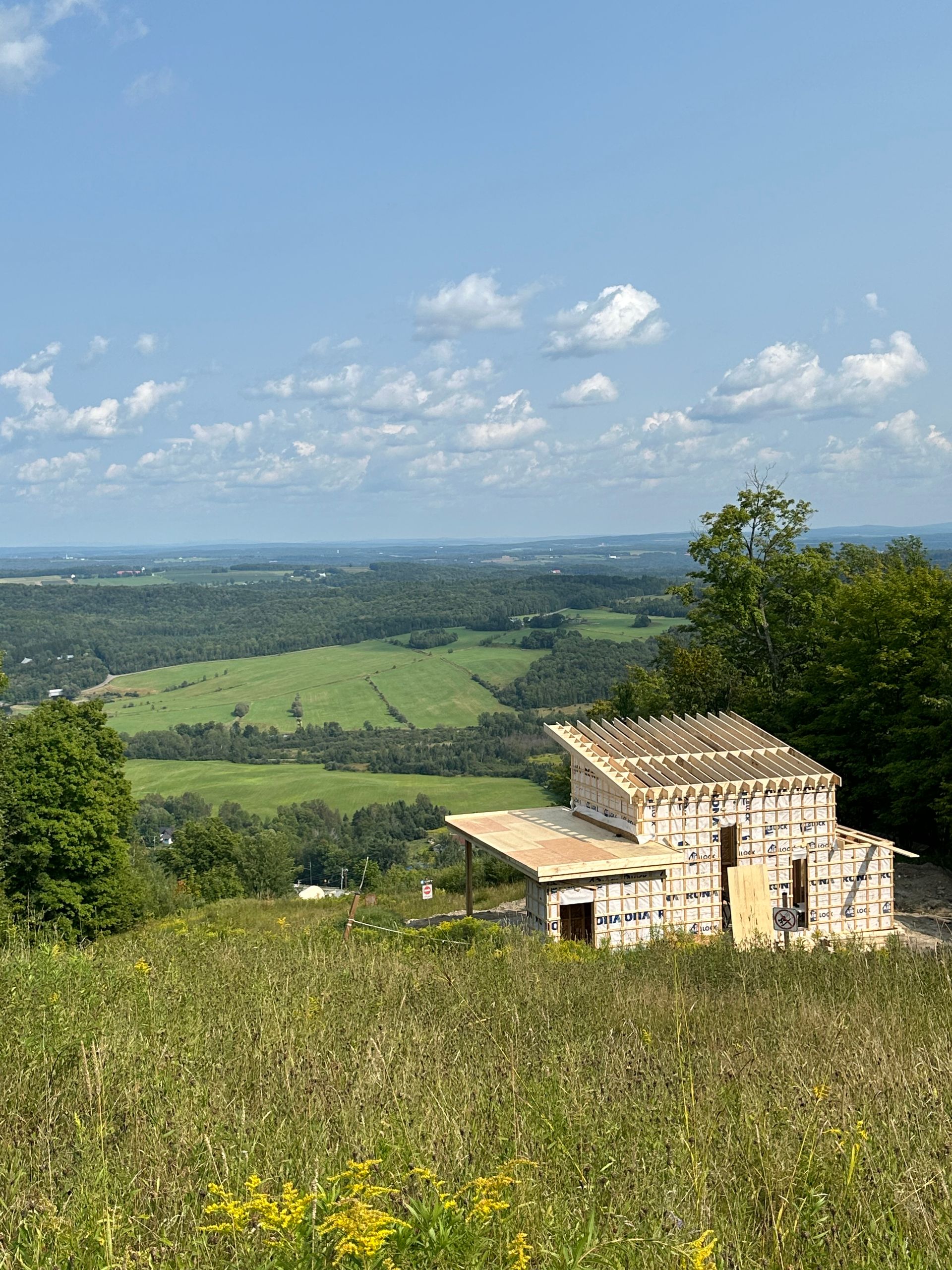 Construction d'un bâtiment au sommet d'une colline surplombant une vallée, ciel bleu avec des nuages.