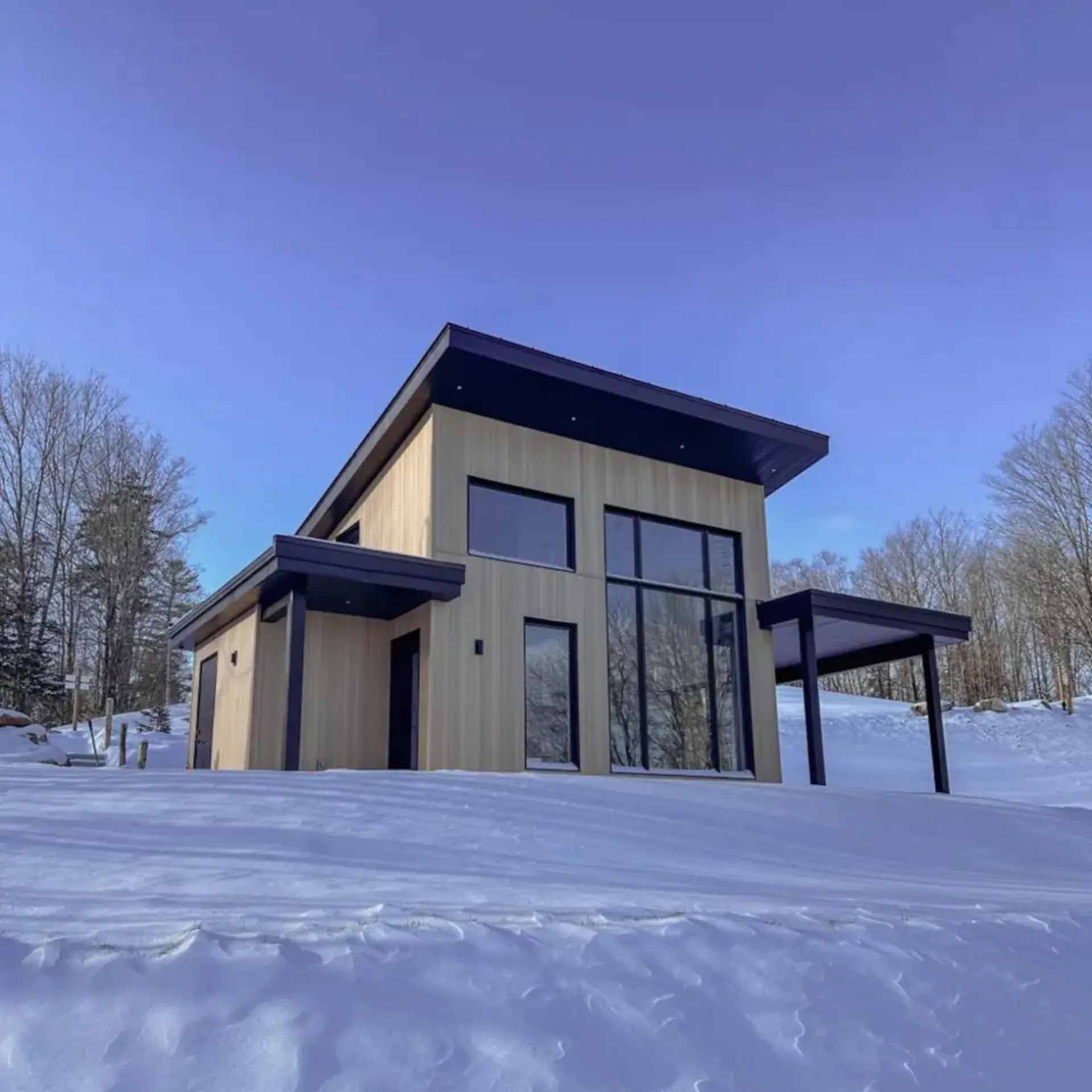 Chalet moderne dans un paysage enneigé, avec bardage en bois clair et finitions foncées.