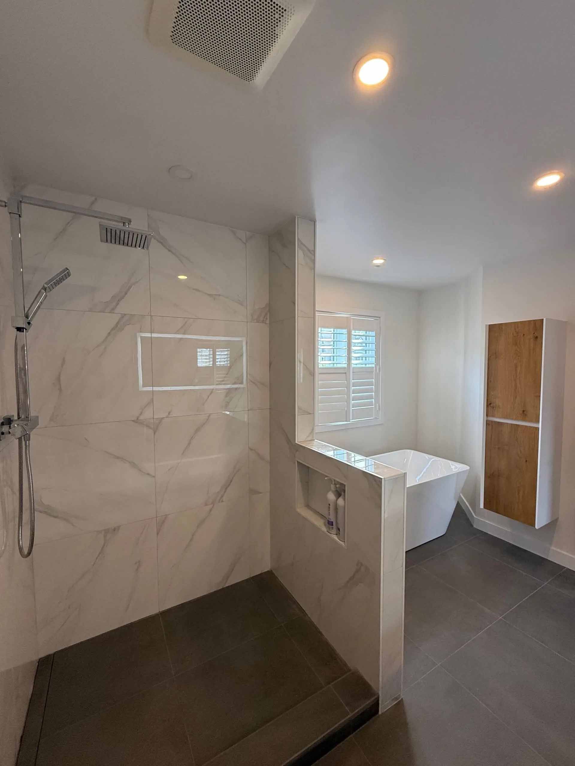 Salle de bains moderne avec douche en marbre, sol gris, baignoire blanche et meuble en bois.