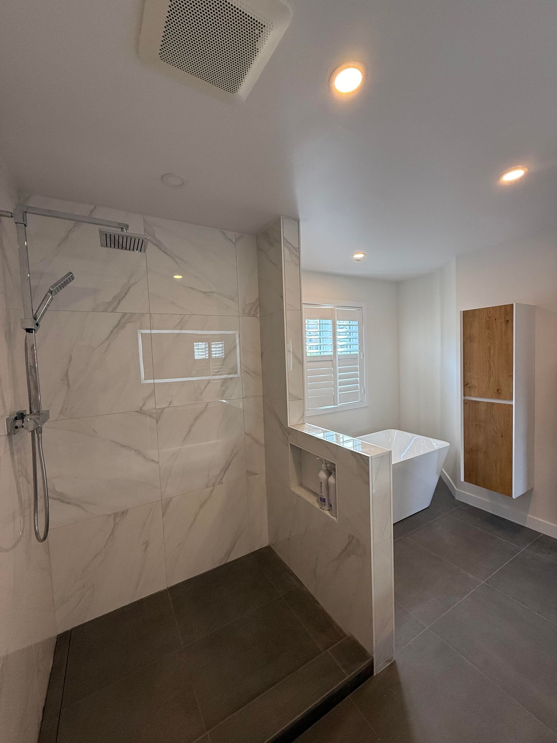 Salle de bains moderne avec douche en marbre blanc, sol en carrelage gris, baignoire blanche et meuble de rangement en bois.