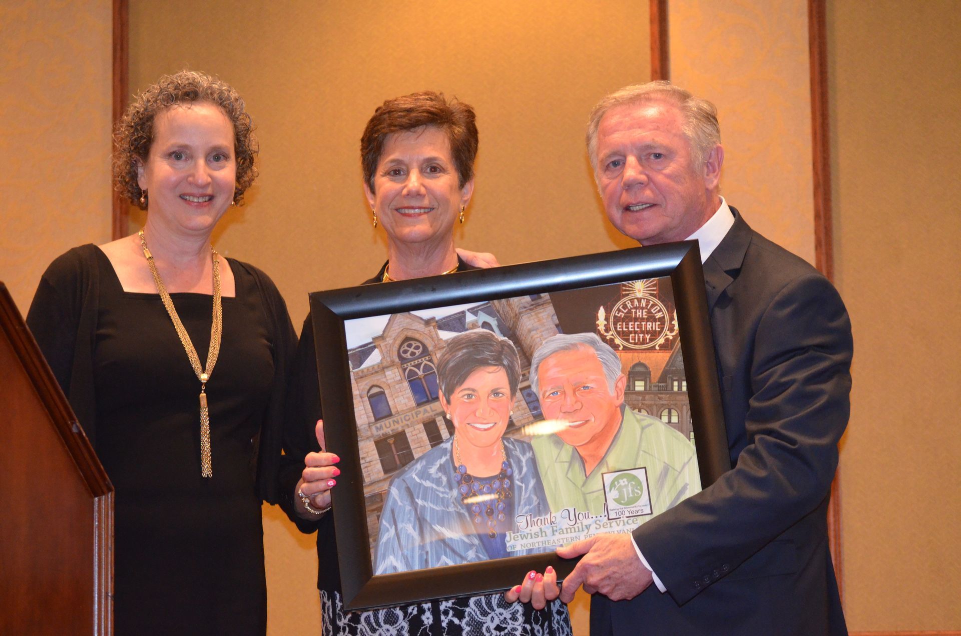 Three people holding a framed portrait; they appear to be at an event.