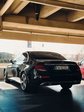 Black sedan parked under an overpass, viewed from the rear in daylight.