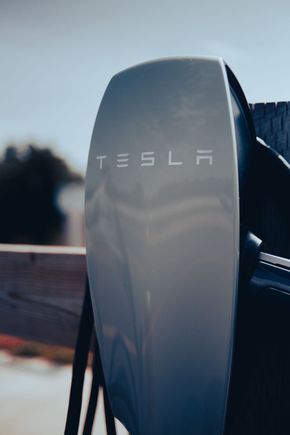 Tesla electric vehicle charging connector close-up with the Tesla logo outdoors