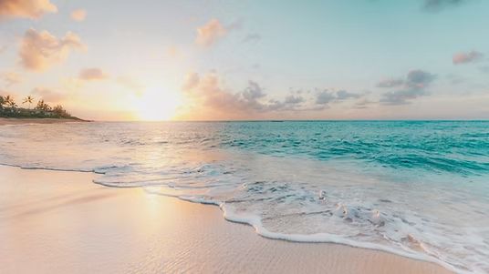 Sunlit beach with gentle turquoise waves and pastel sky at sunrise