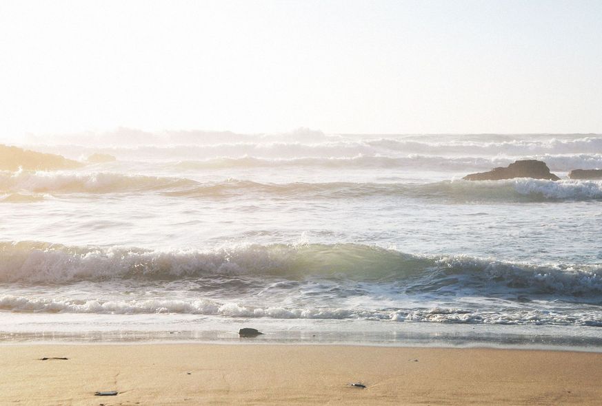 Sunlit beach with gentle waves and a rocky outcrop in the distance