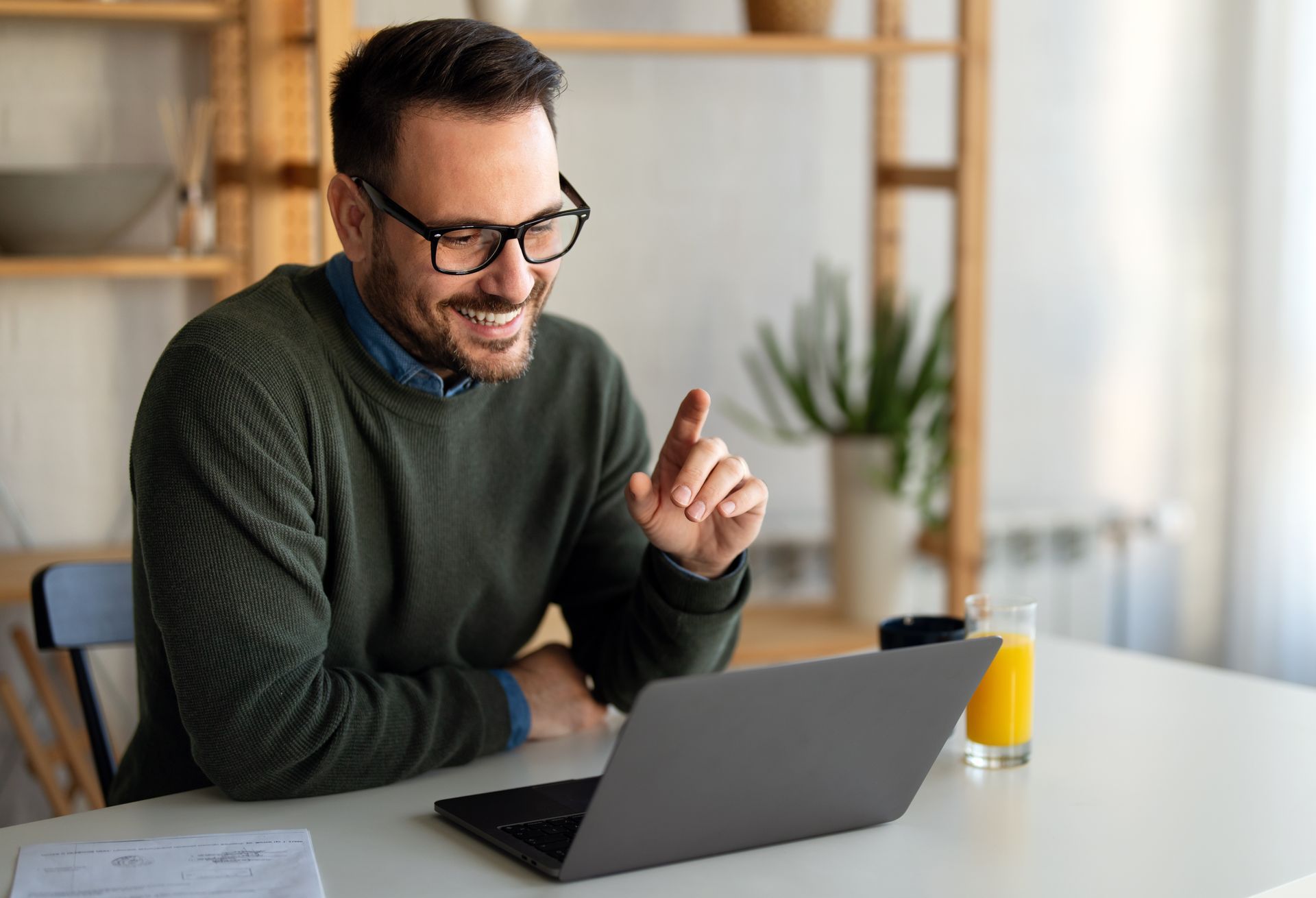 Two people discuss documents at a white office desk with a laptop and chart papers.