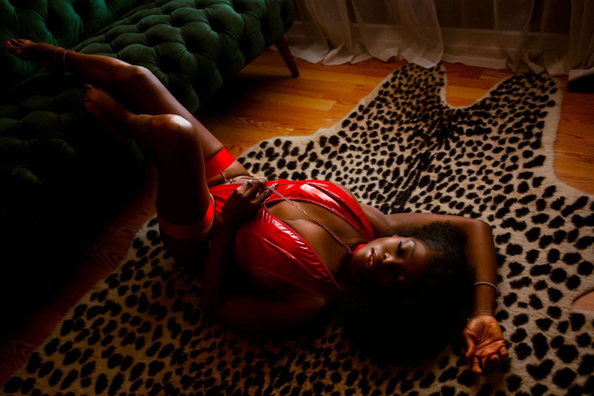 Woman in red lingerie reclining on a leopard-print rug beside a green sofa.