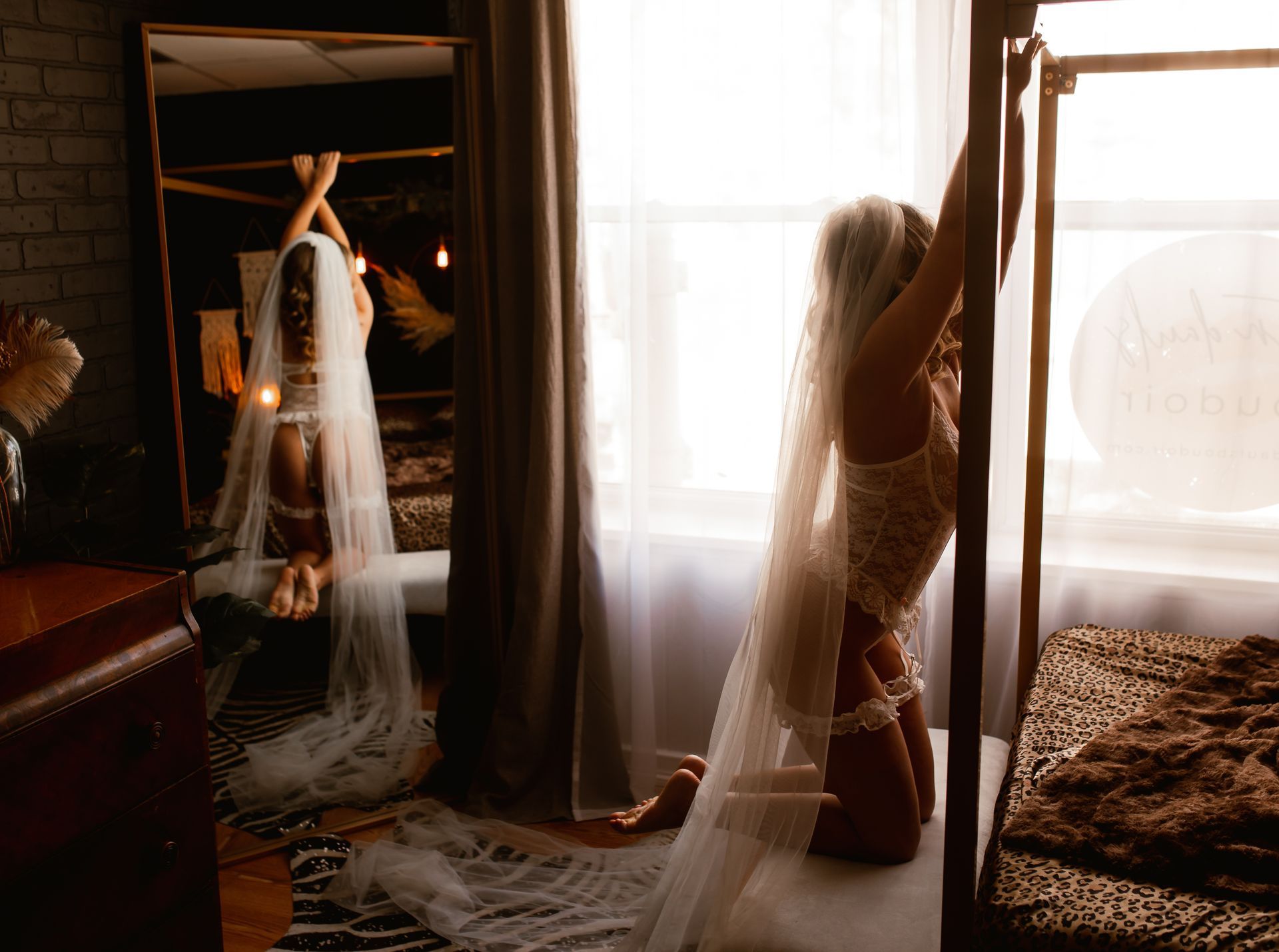 A woman in a wedding dress and veil is kneeling on a bed in front of a window.