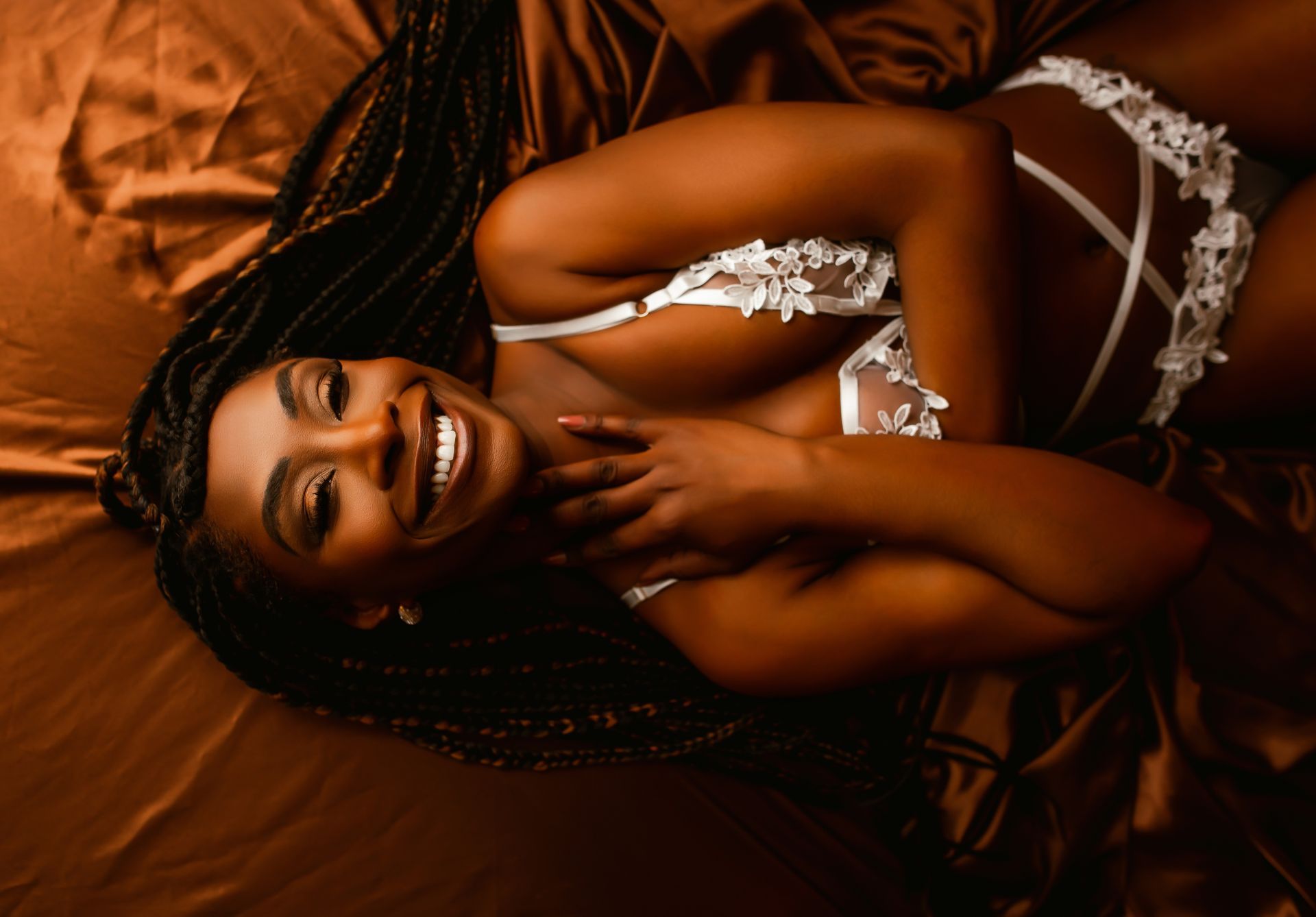 A woman in lingerie is laying on a bed and smiling.