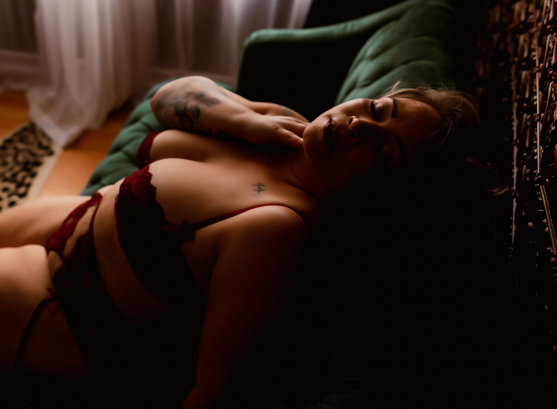 Person reclining on a green sofa in warm, dim light, wearing a red top and looking toward the camera.