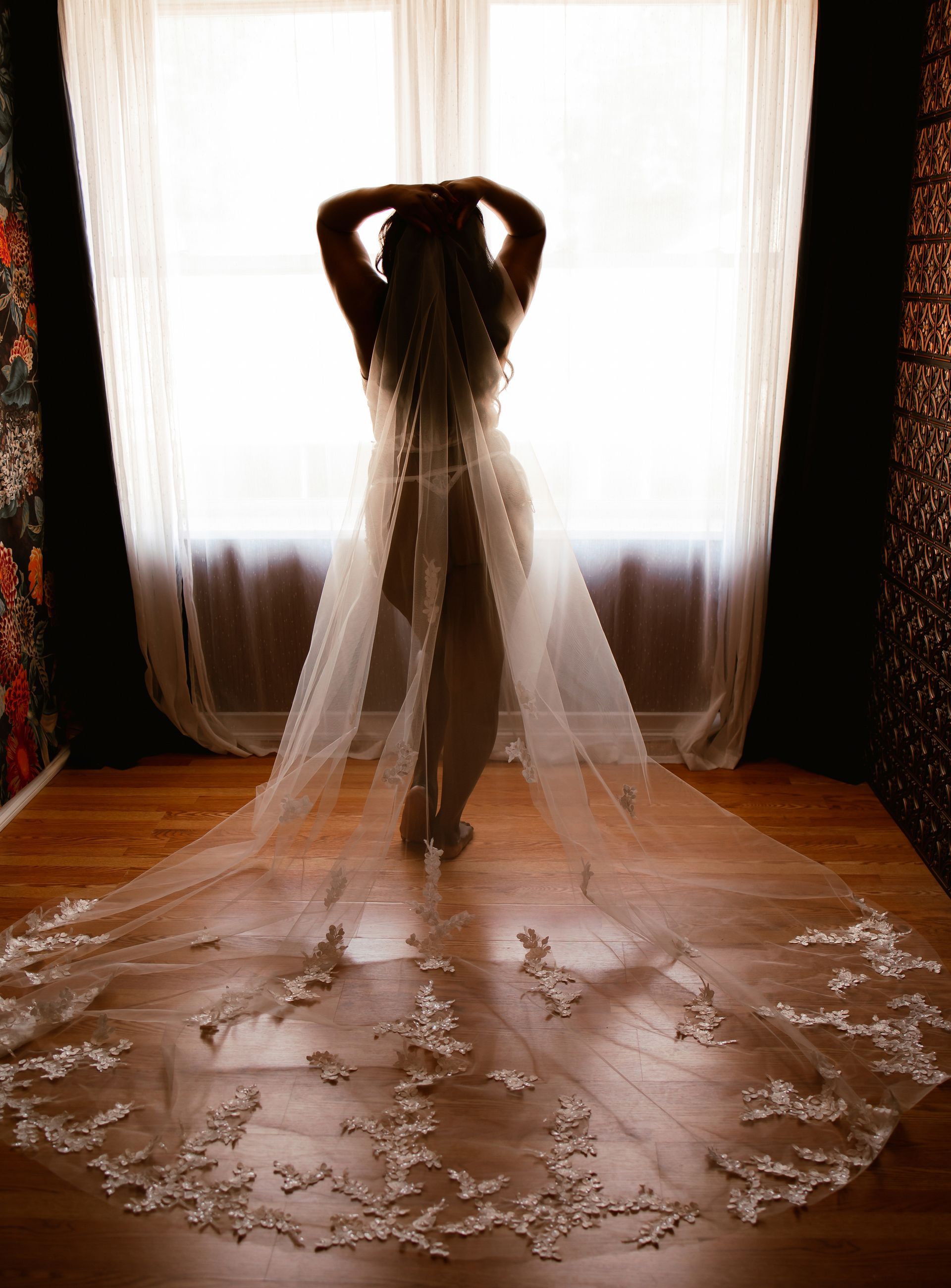 A woman in a wedding dress and veil is standing in front of a window.