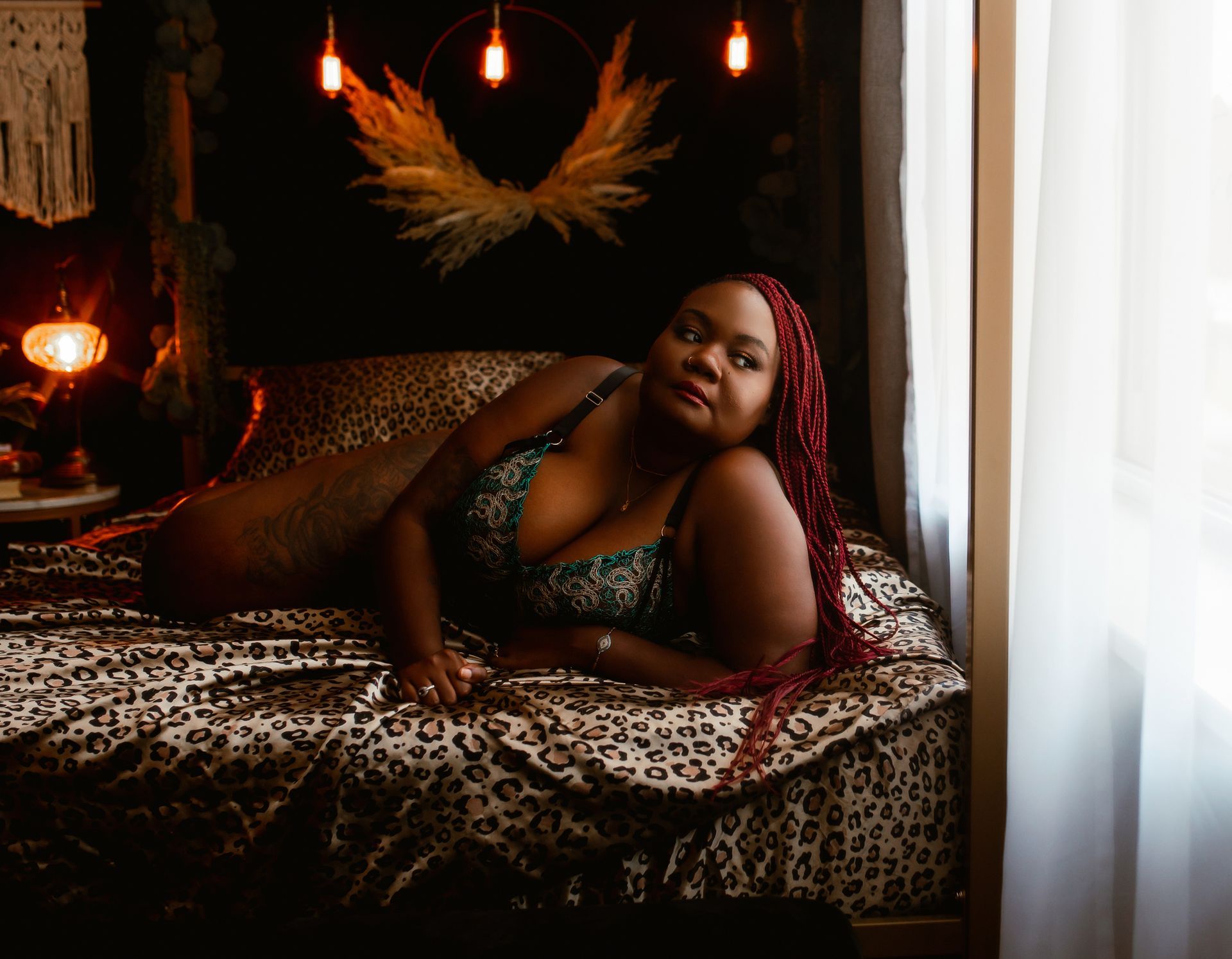 A woman in lingerie is laying on a bed in front of a window.