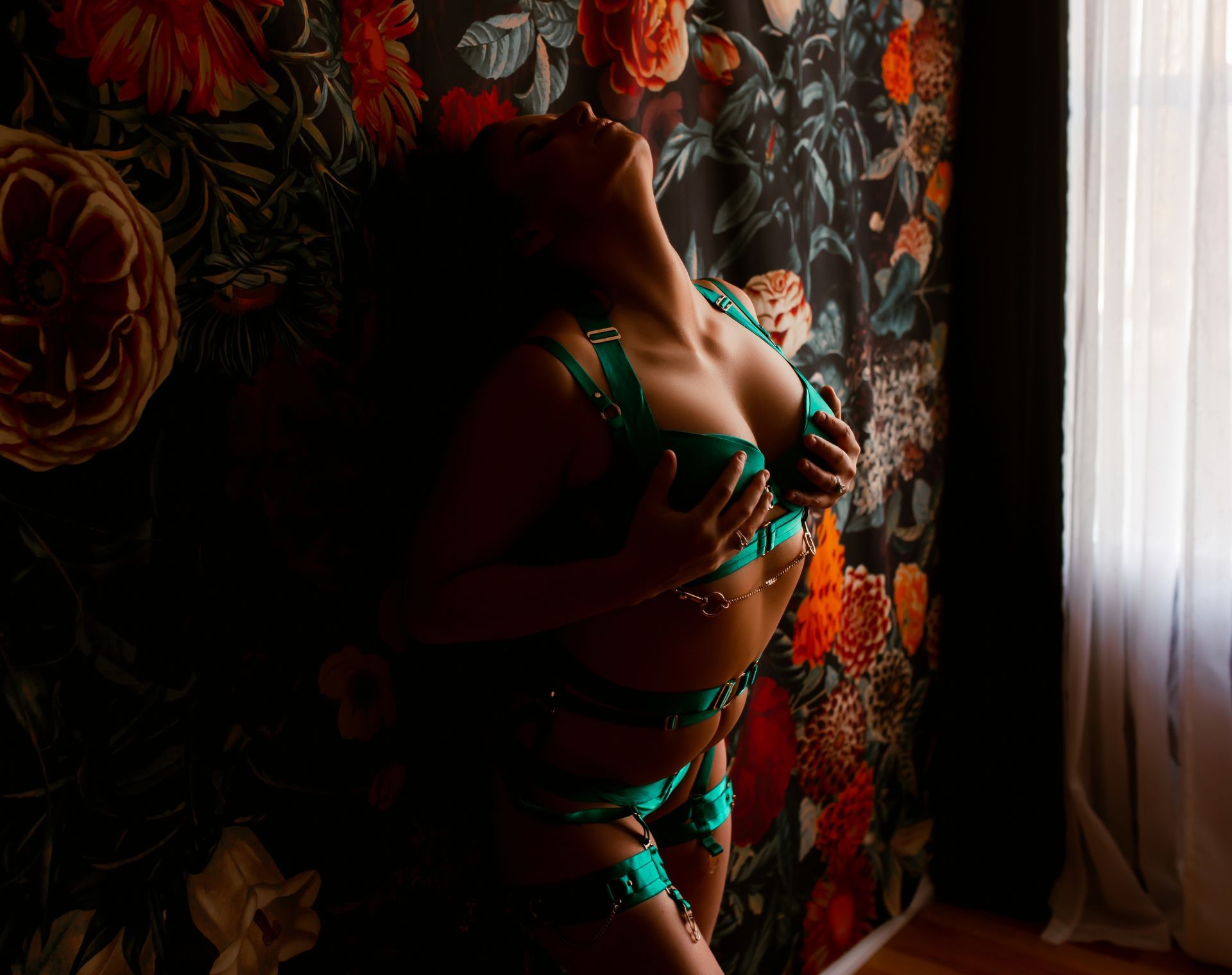 A woman in lingerie is standing in front of a floral wallpaper.