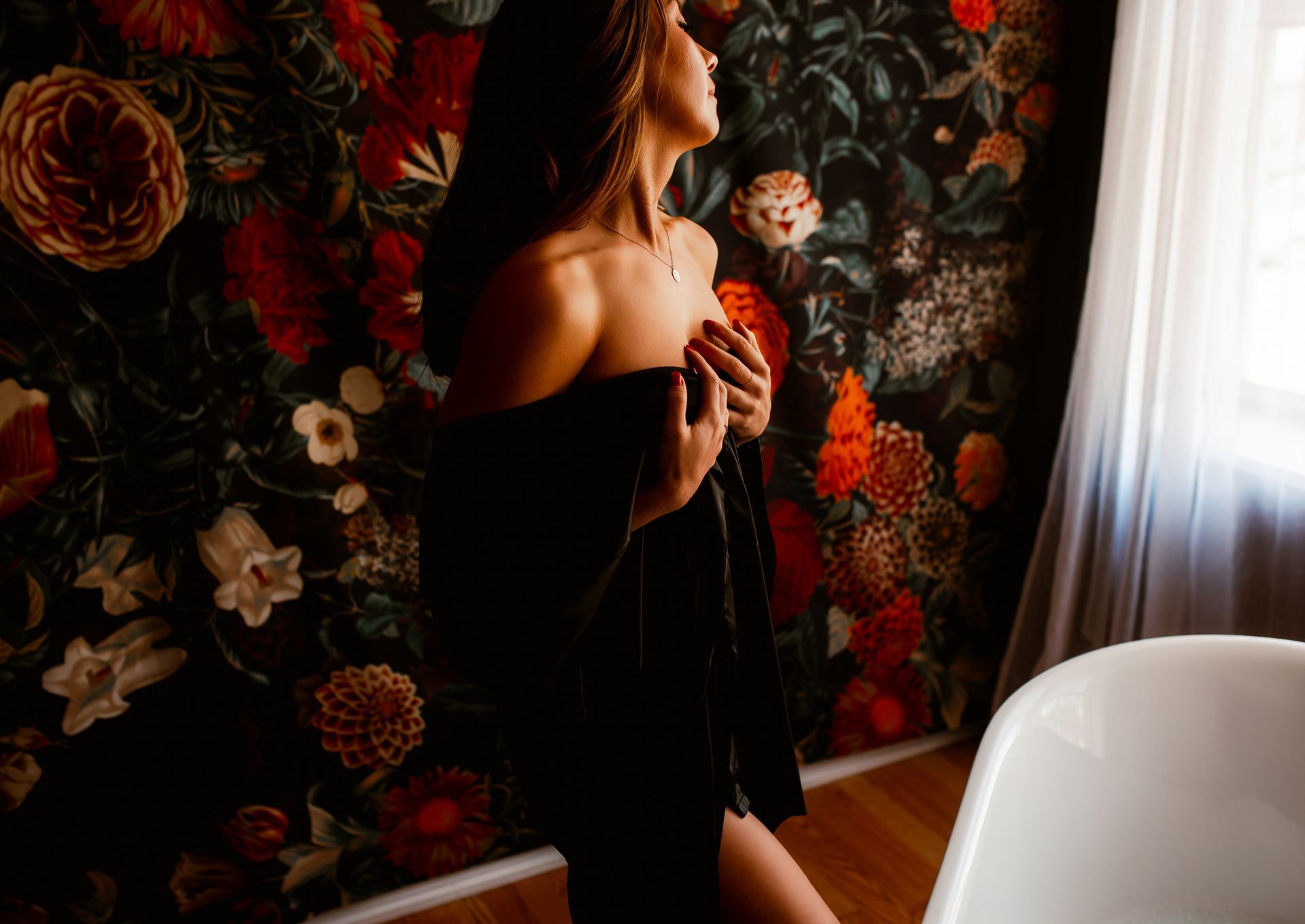 A woman in a black dress is standing next to a bathtub in a bathroom.