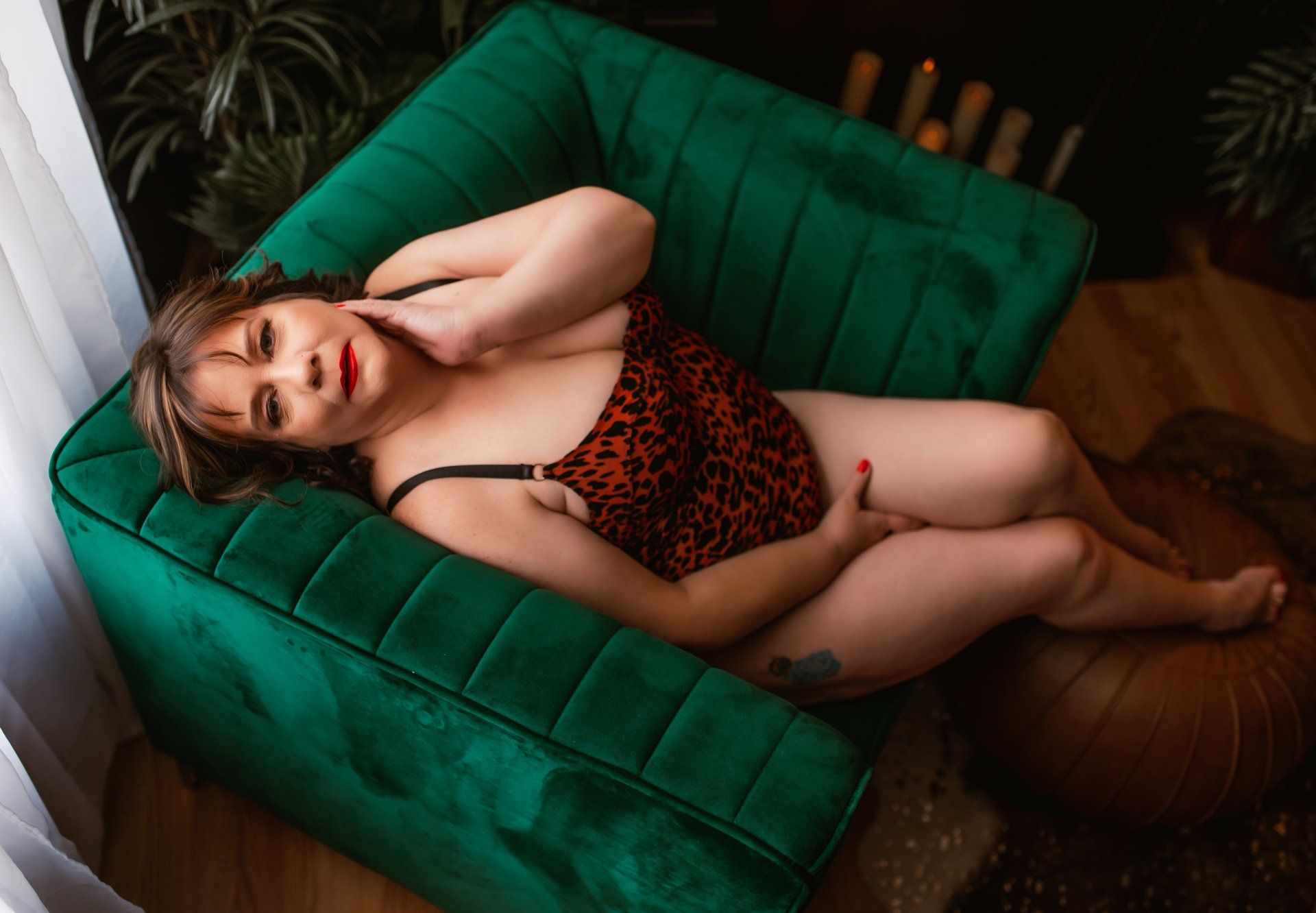 Woman reclining on a green chair in a leopard-print dress, hand behind head, indoors.