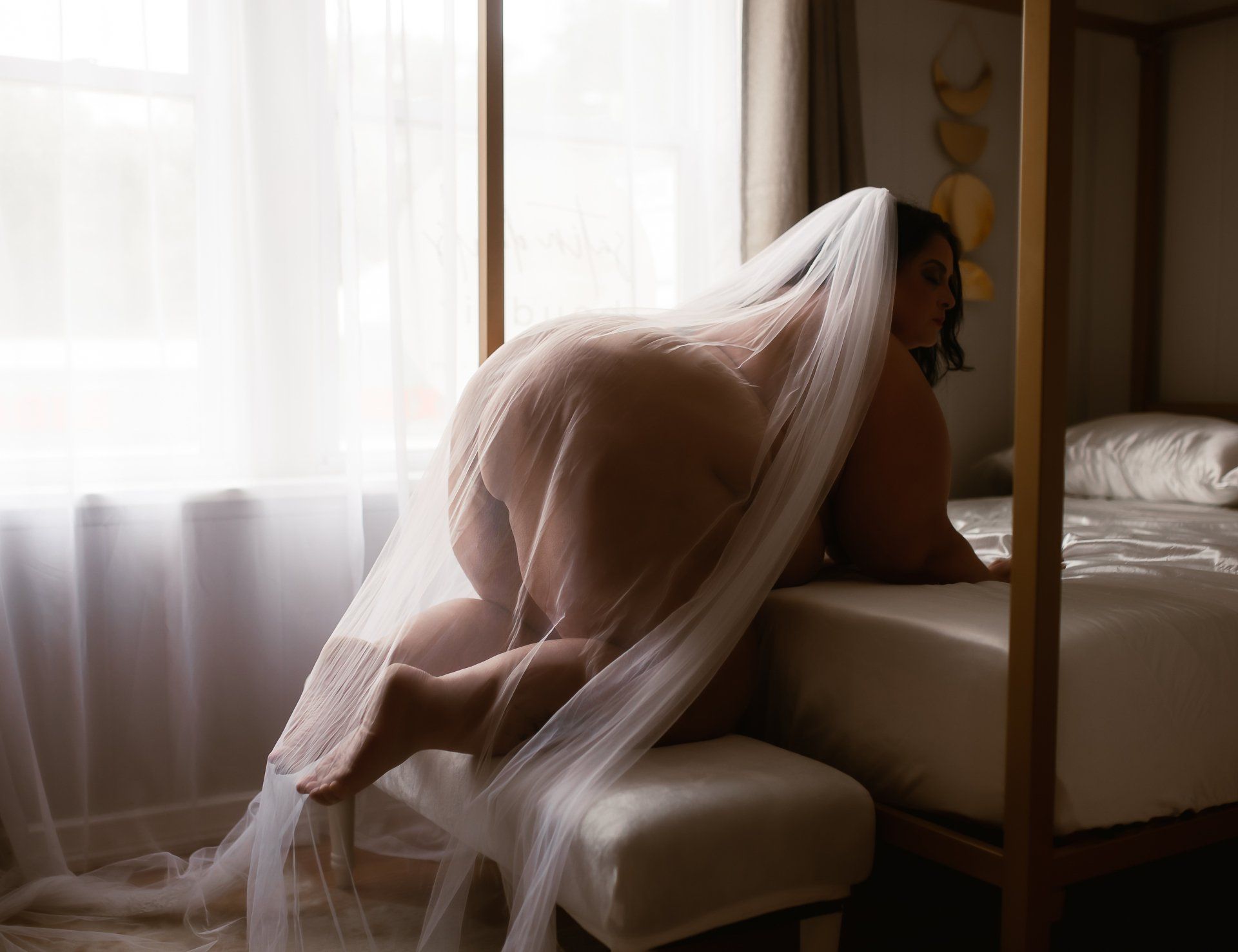 A woman in a wedding dress and veil is kneeling on a bed.