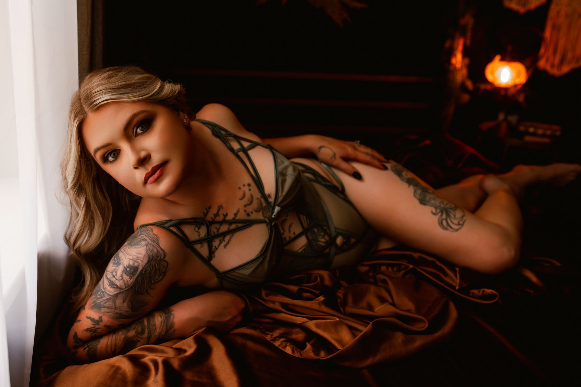 A woman in lingerie is laying on a bed next to a window.