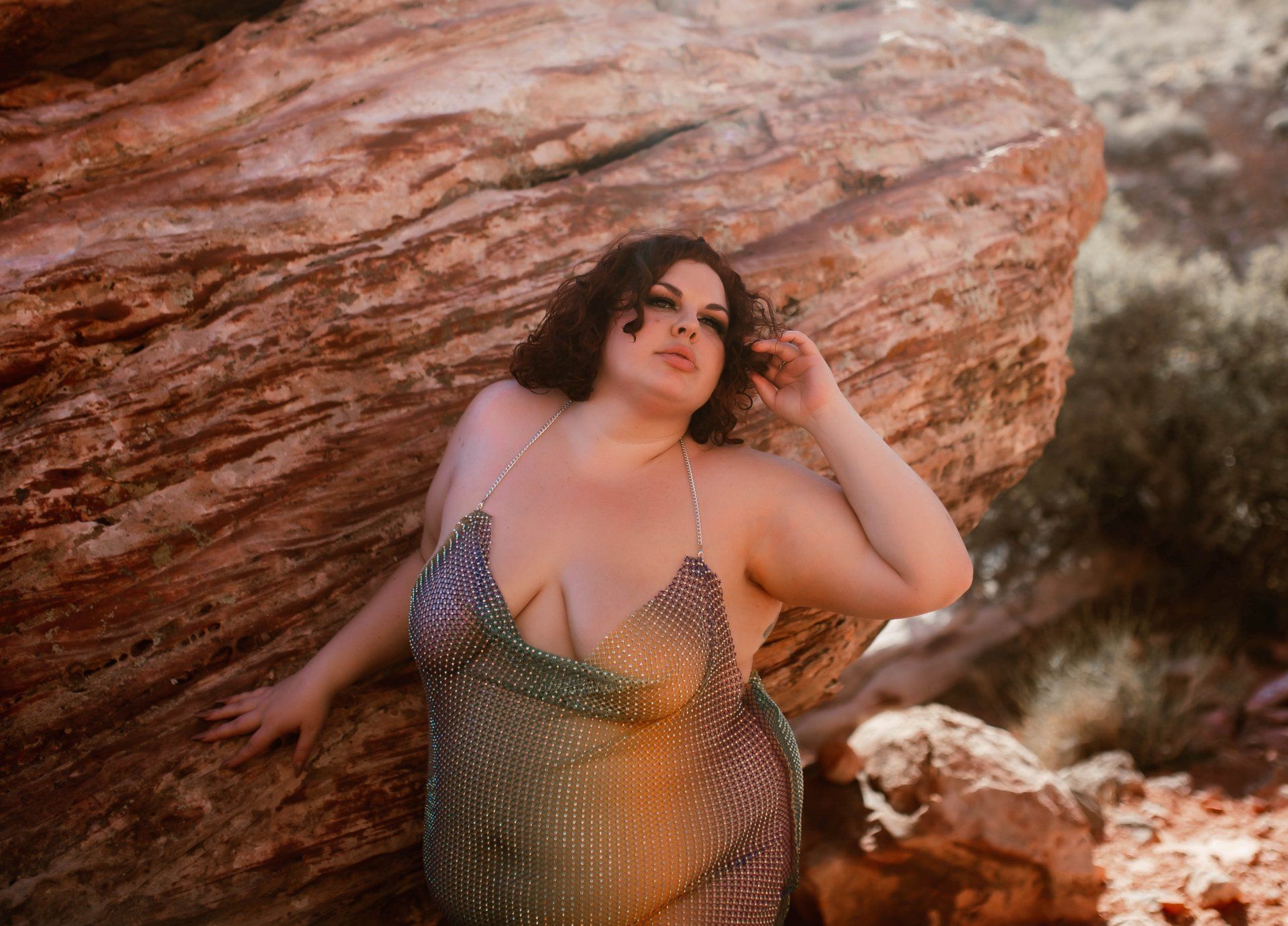 A woman in a rainbow dress is standing next to a large rock.