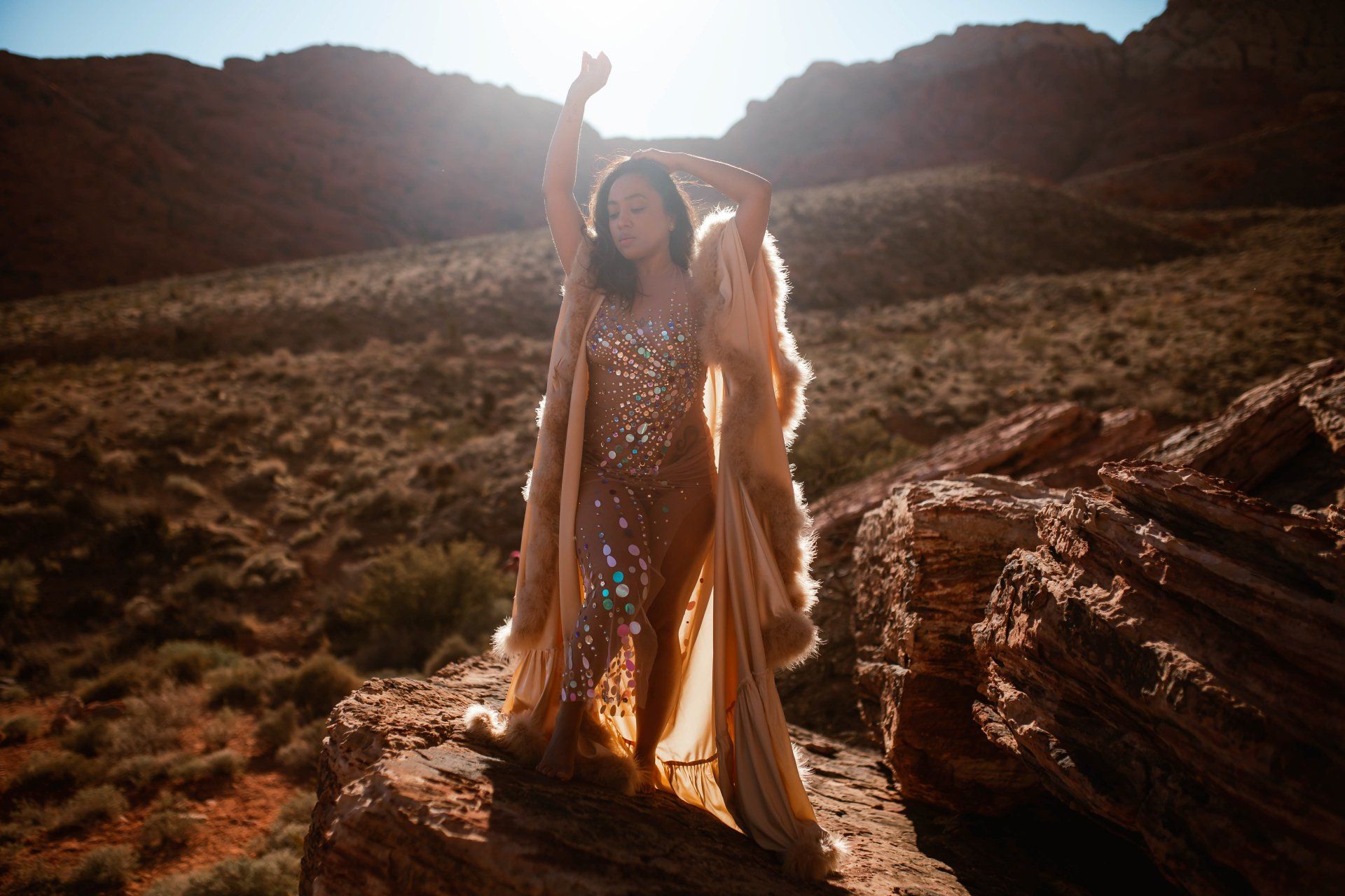 A woman in a long dress is standing on a rock in the desert.