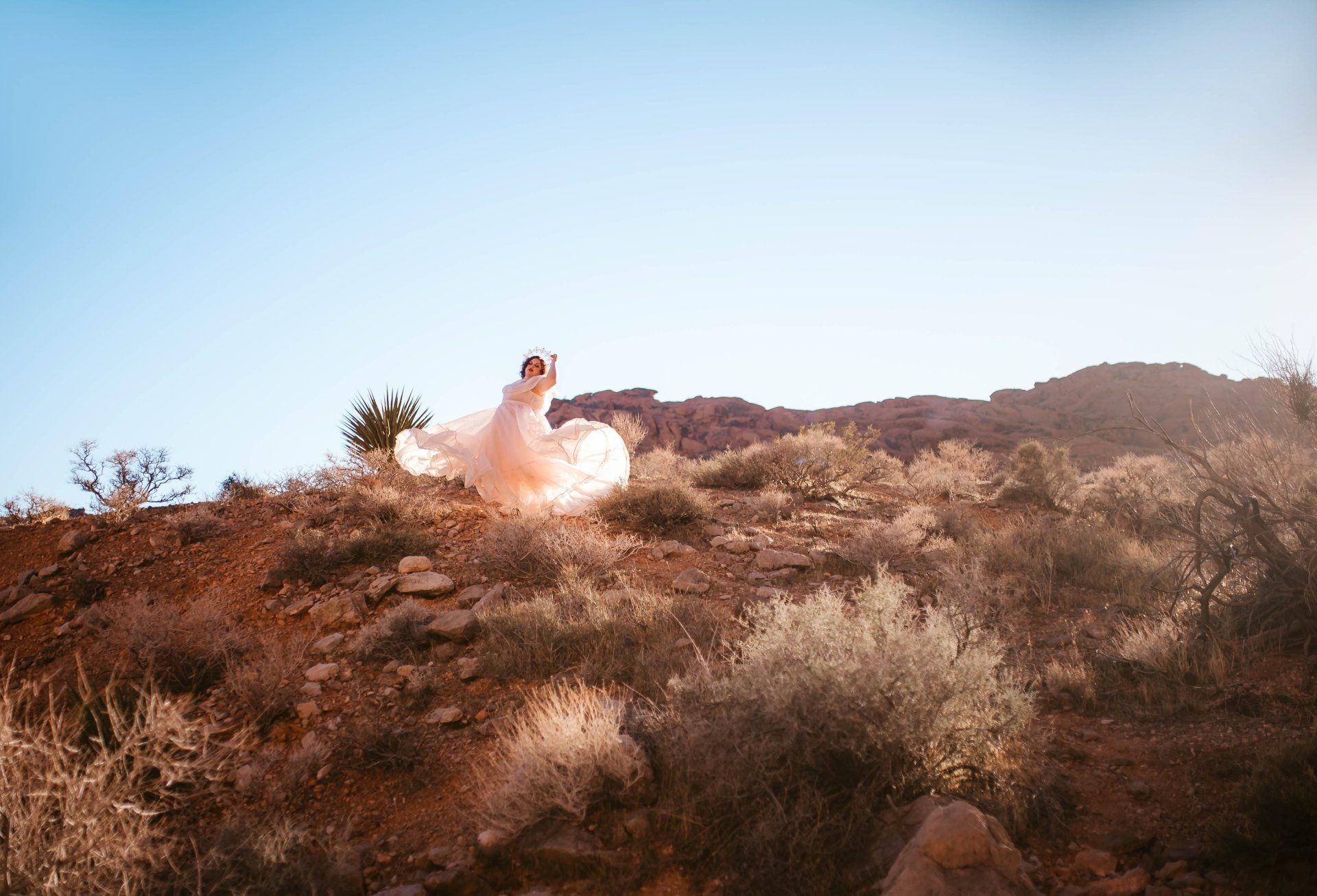 A woman in a wedding dress is standing on top of a desert hill.