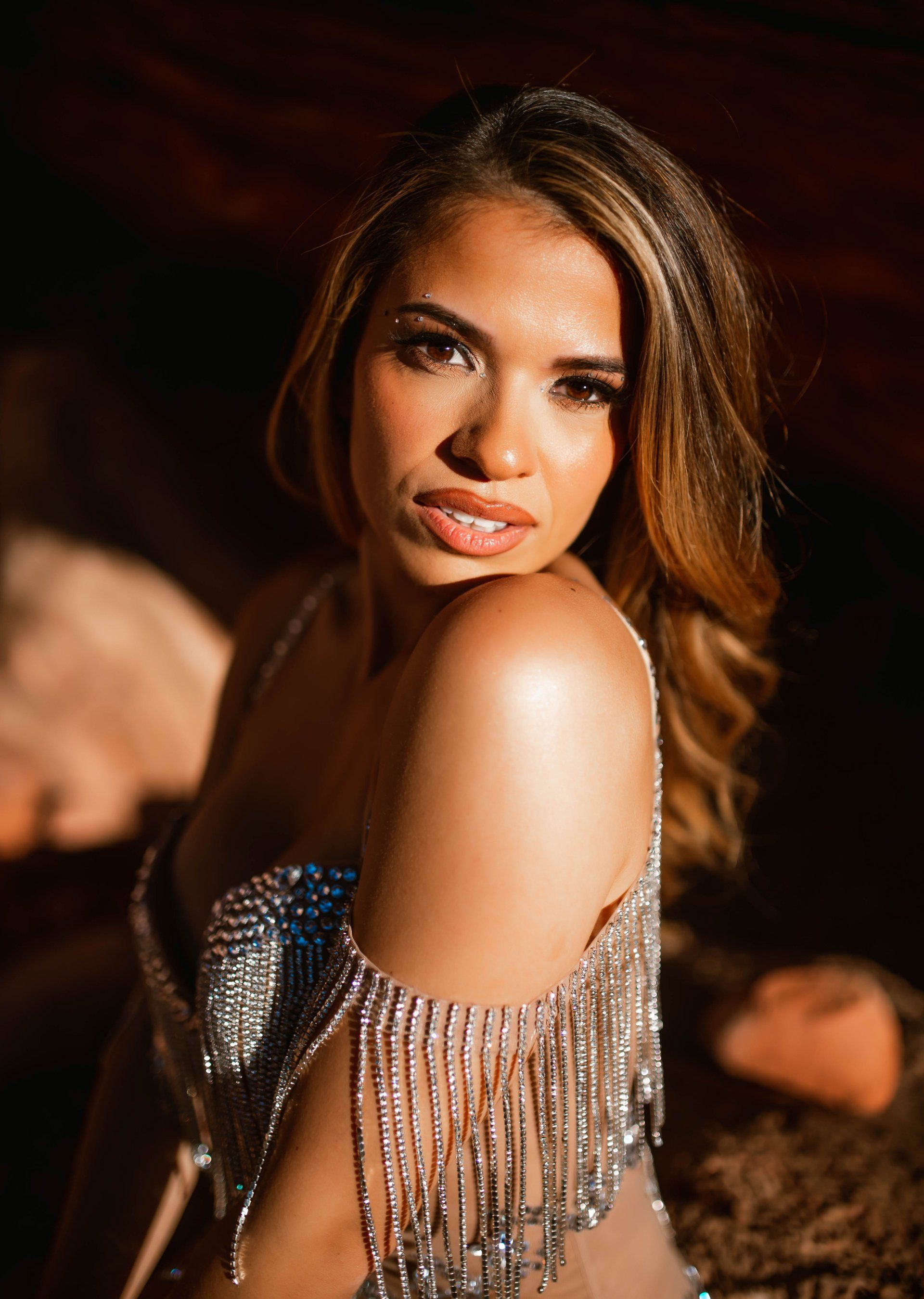 A woman in a silver dress is sitting on the floor and looking at the camera.