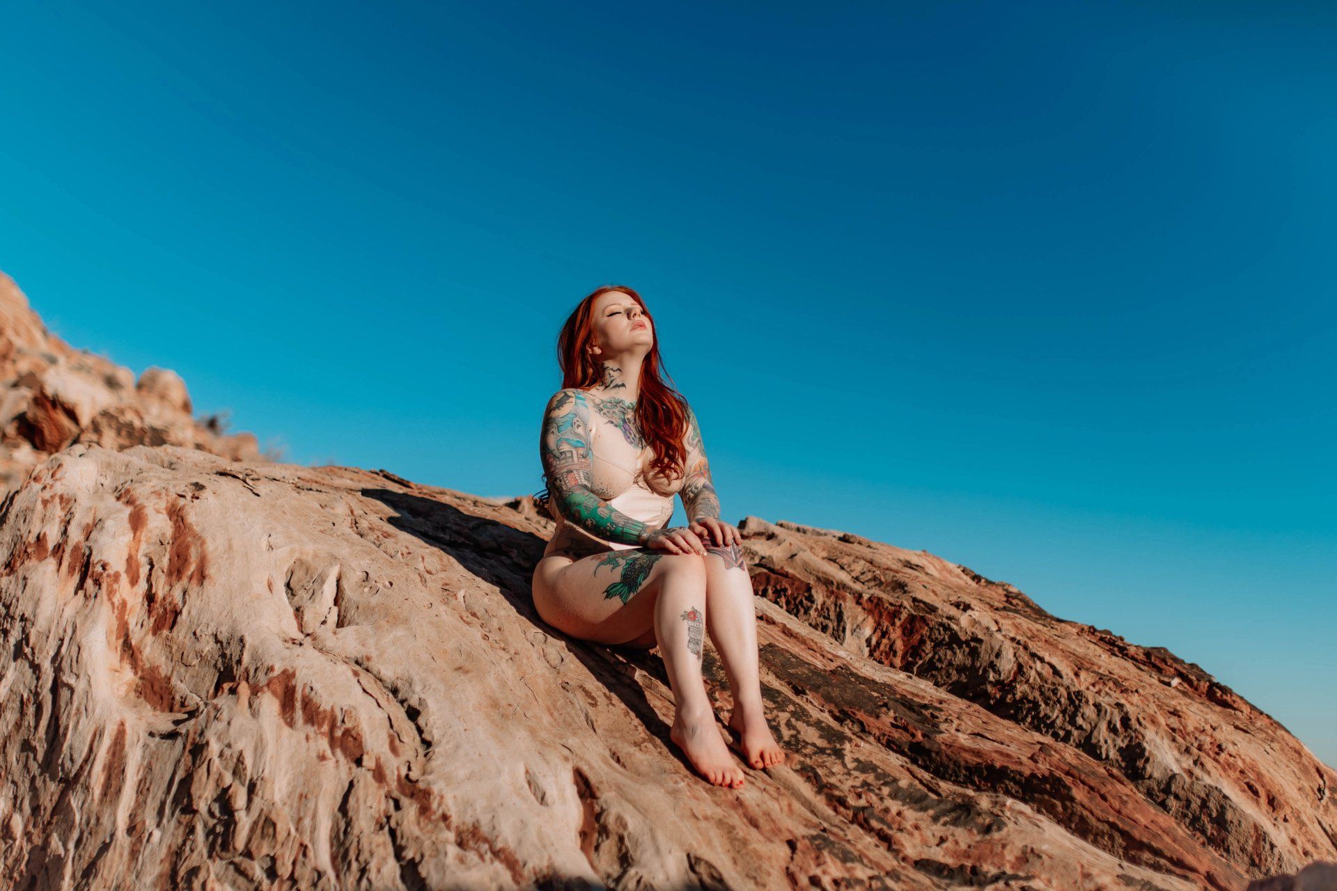 A woman is sitting on top of a rock looking up at the sky.