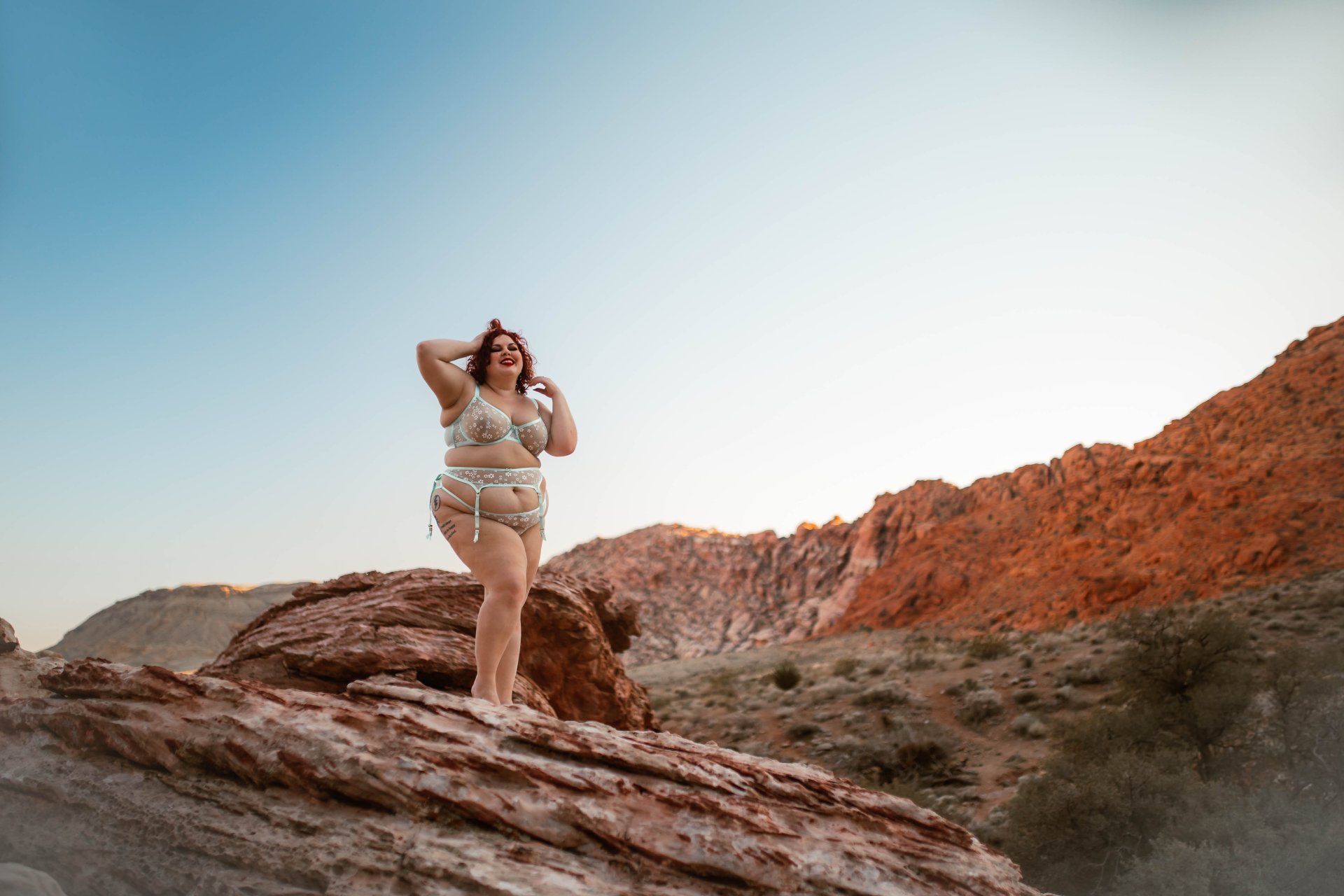 A woman in a bikini is standing on top of a rock in the desert.