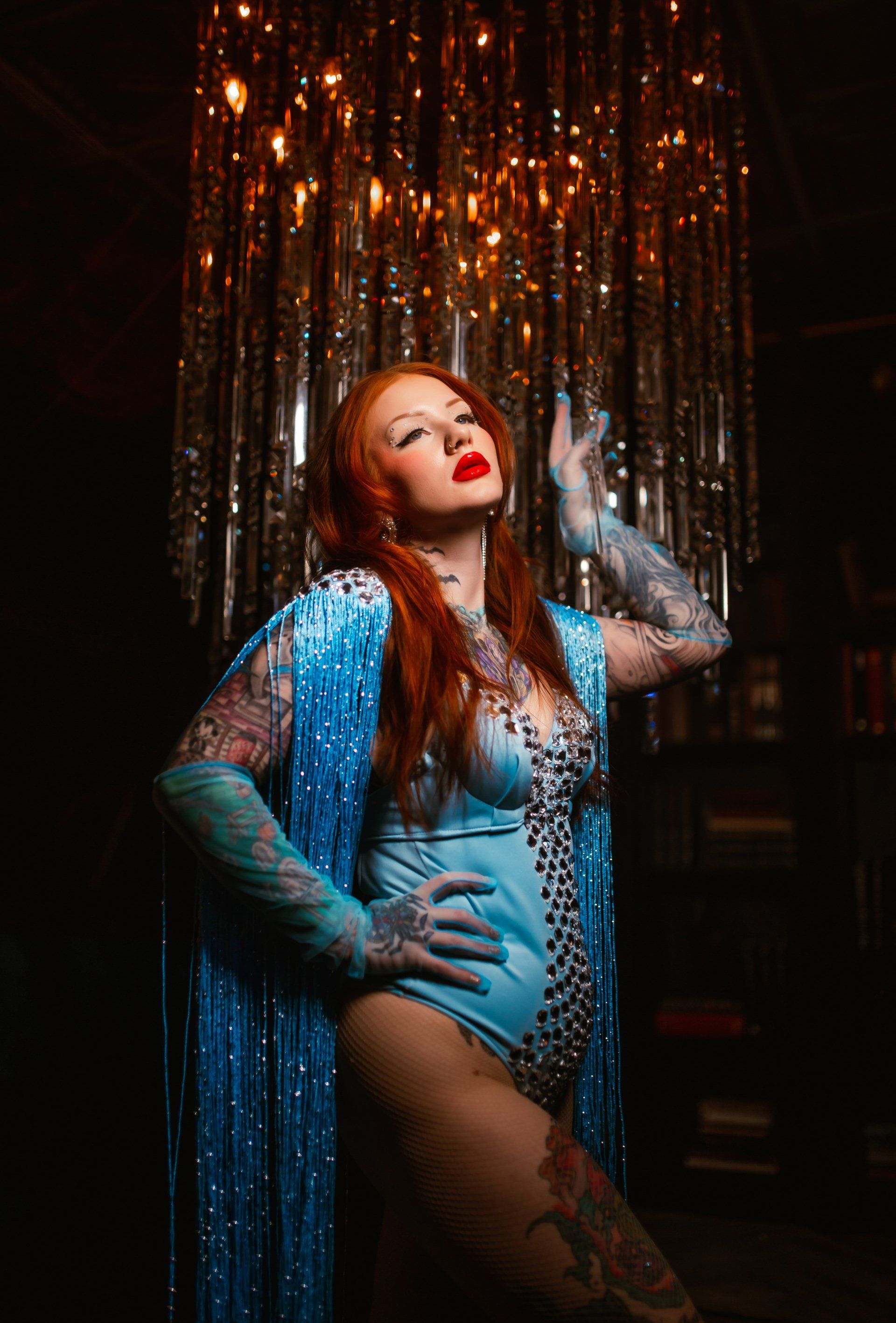 A woman in a blue bodysuit and gloves is standing in front of a curtain.