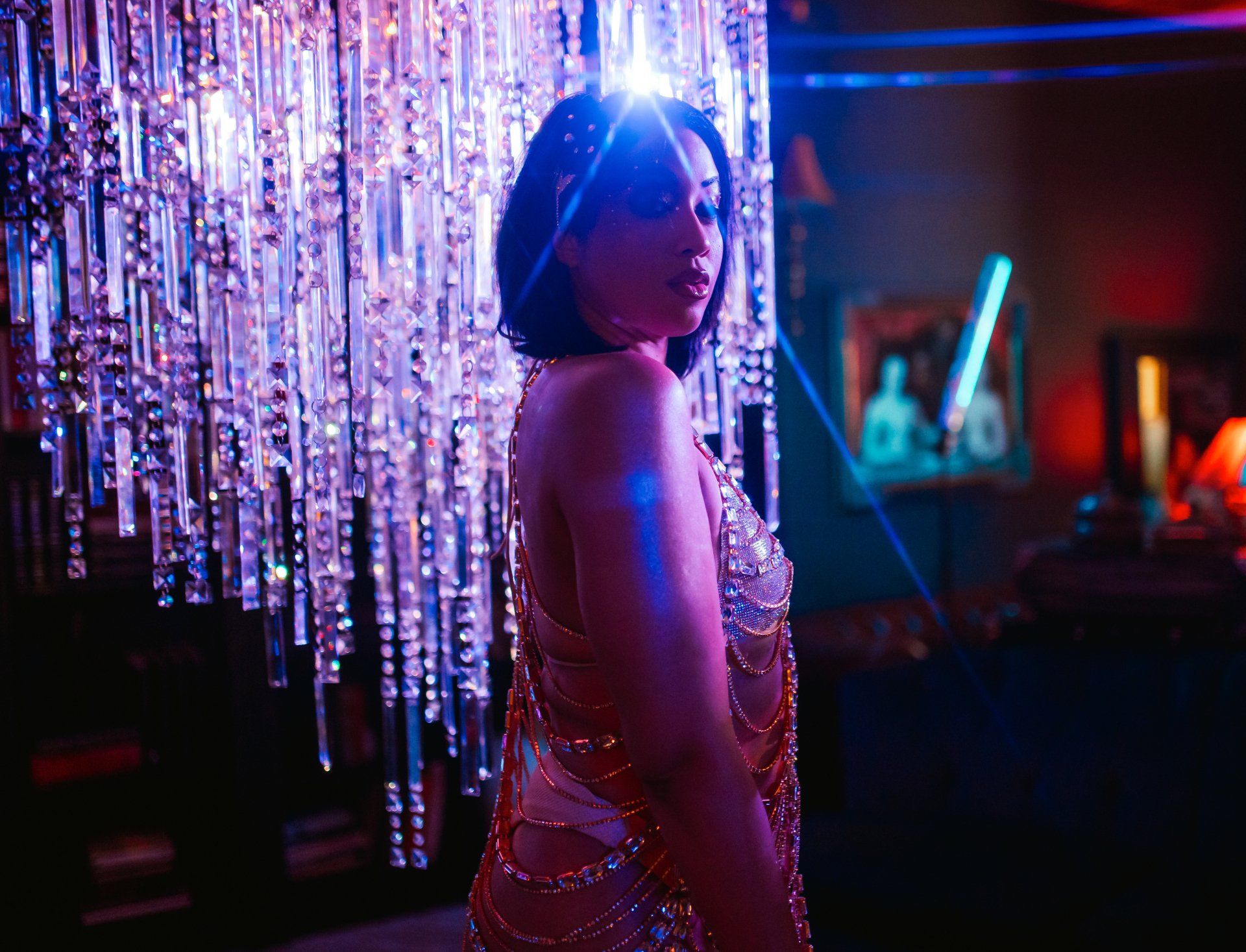 A woman in a dress is standing in front of a chandelier in a dark room.