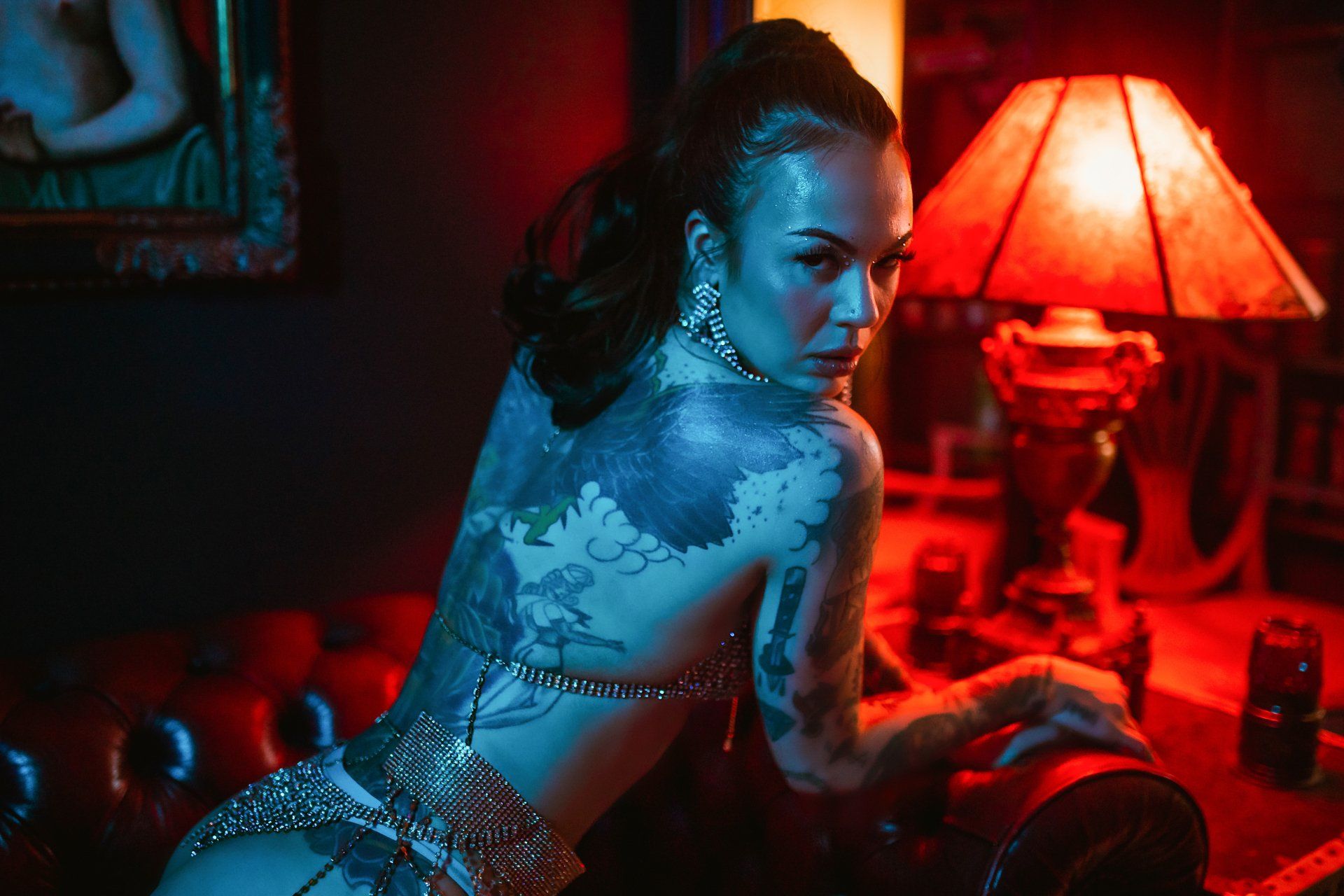 A woman with a lot of tattoos is sitting on a couch in front of a lamp.