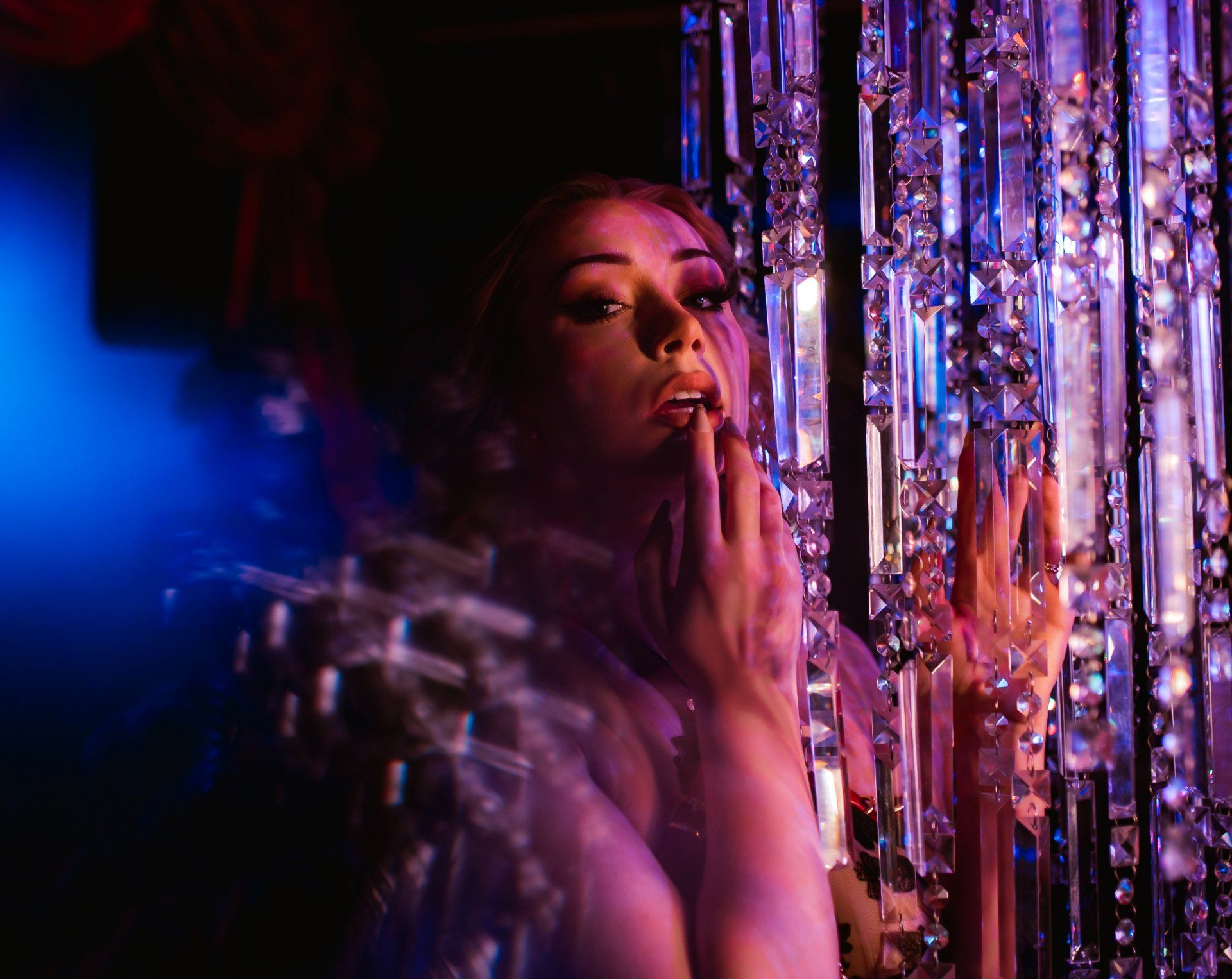 A woman is standing in front of a chandelier in a dark room.