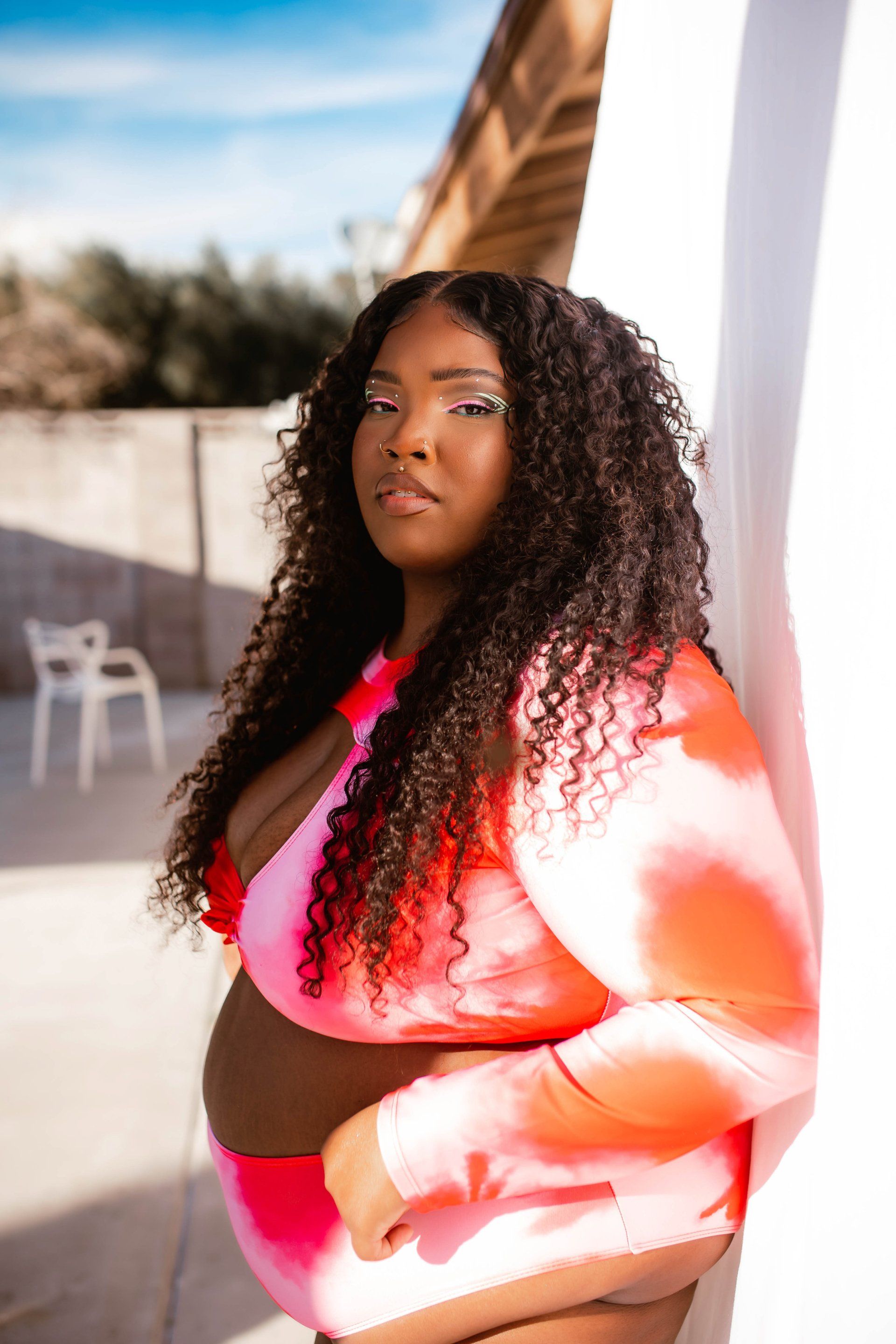A woman in a pink and orange bikini is leaning against a wall.