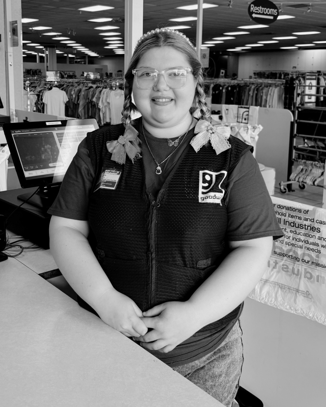 Woman in a vest at a checkout counter, smiling.