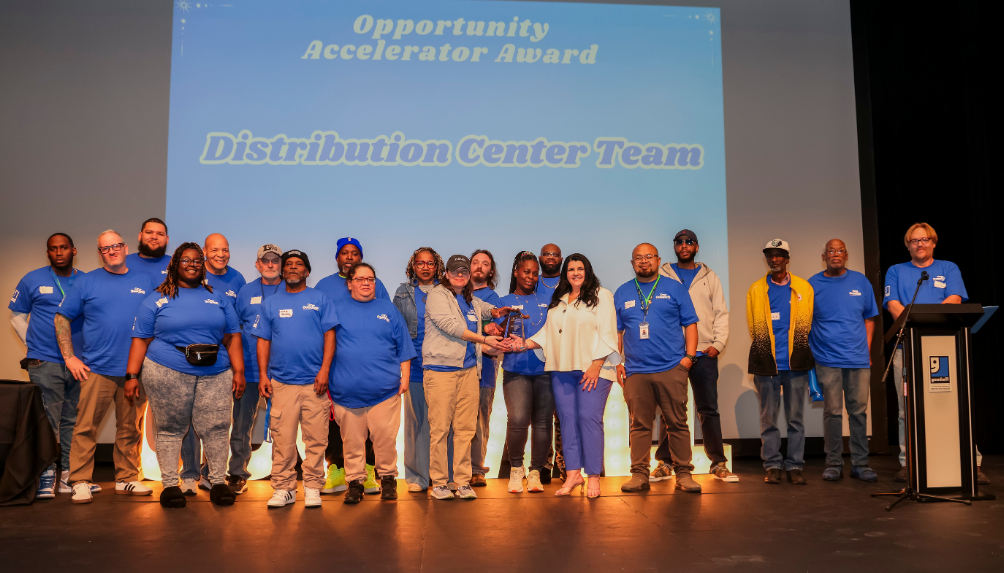Group of employees in blue shirts on stage receiving a Distribution Center Team award at a ceremony