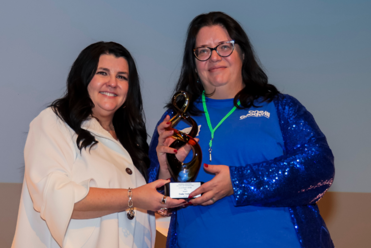 Two women on stage holding a trophy, with “Heather Hutchinson” text at the bottom.