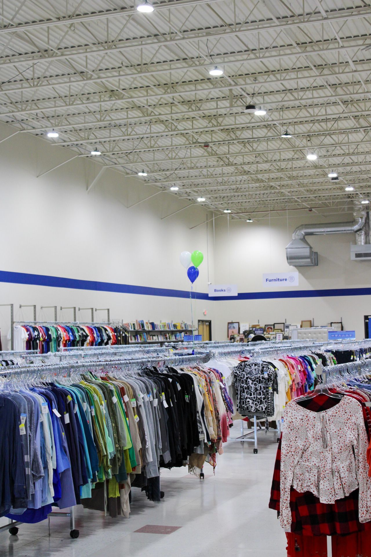 Clothing racks in a brightly lit thrift store, blue and white walls, balloons visible.
