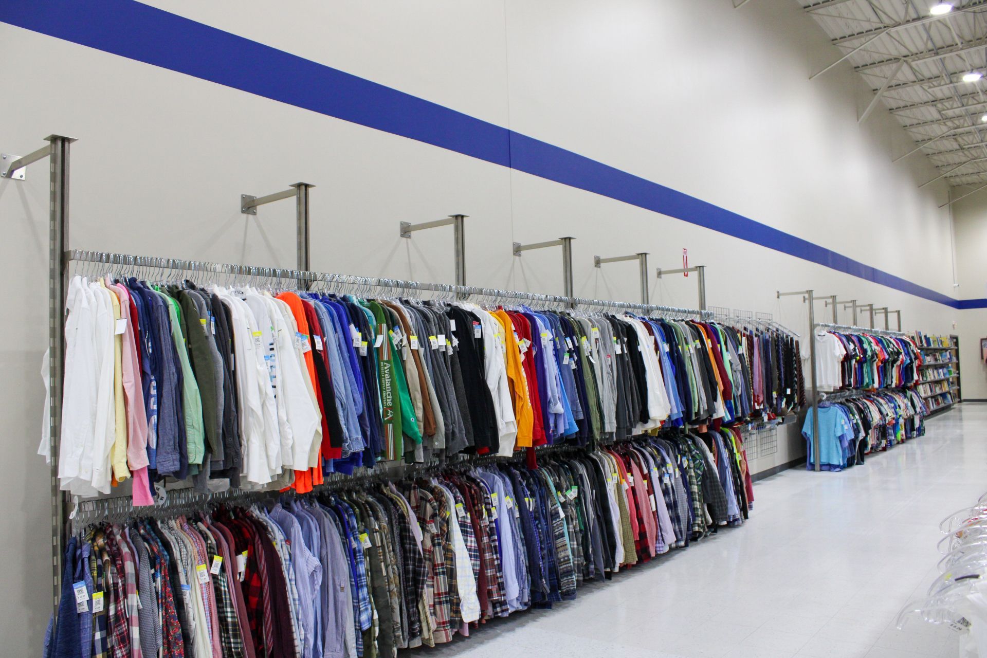 Rows of clothing on racks in a brightly lit retail space with white walls and a blue stripe.