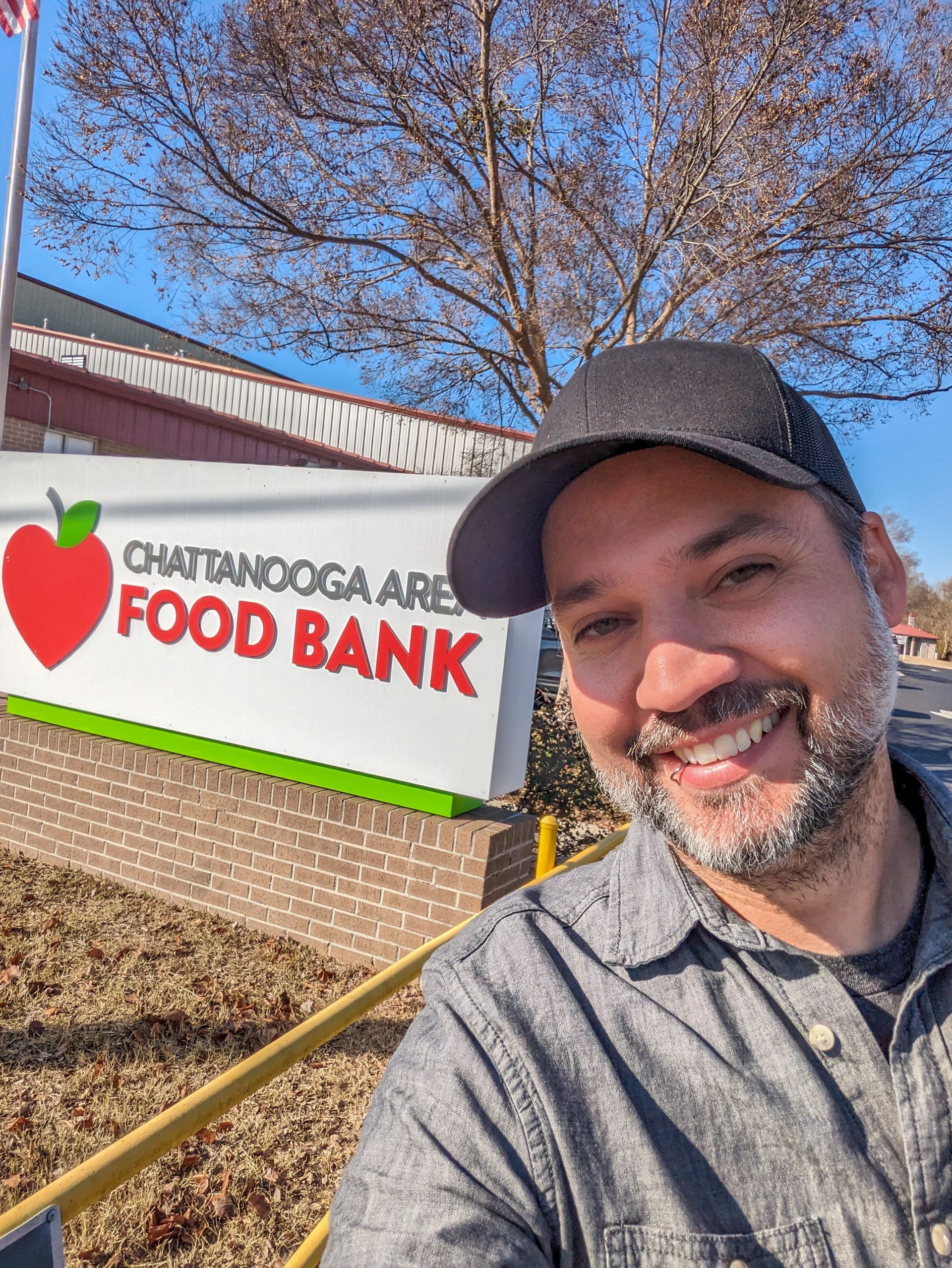 A man is smiling in front of a food bank sign.