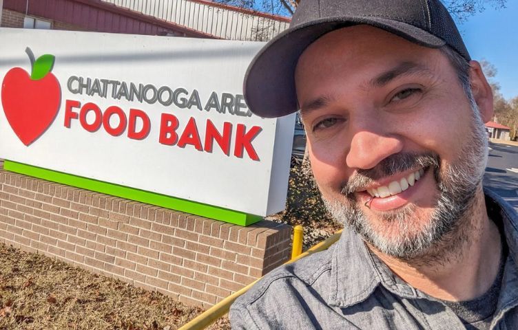 A man is smiling in front of a food bank sign.
